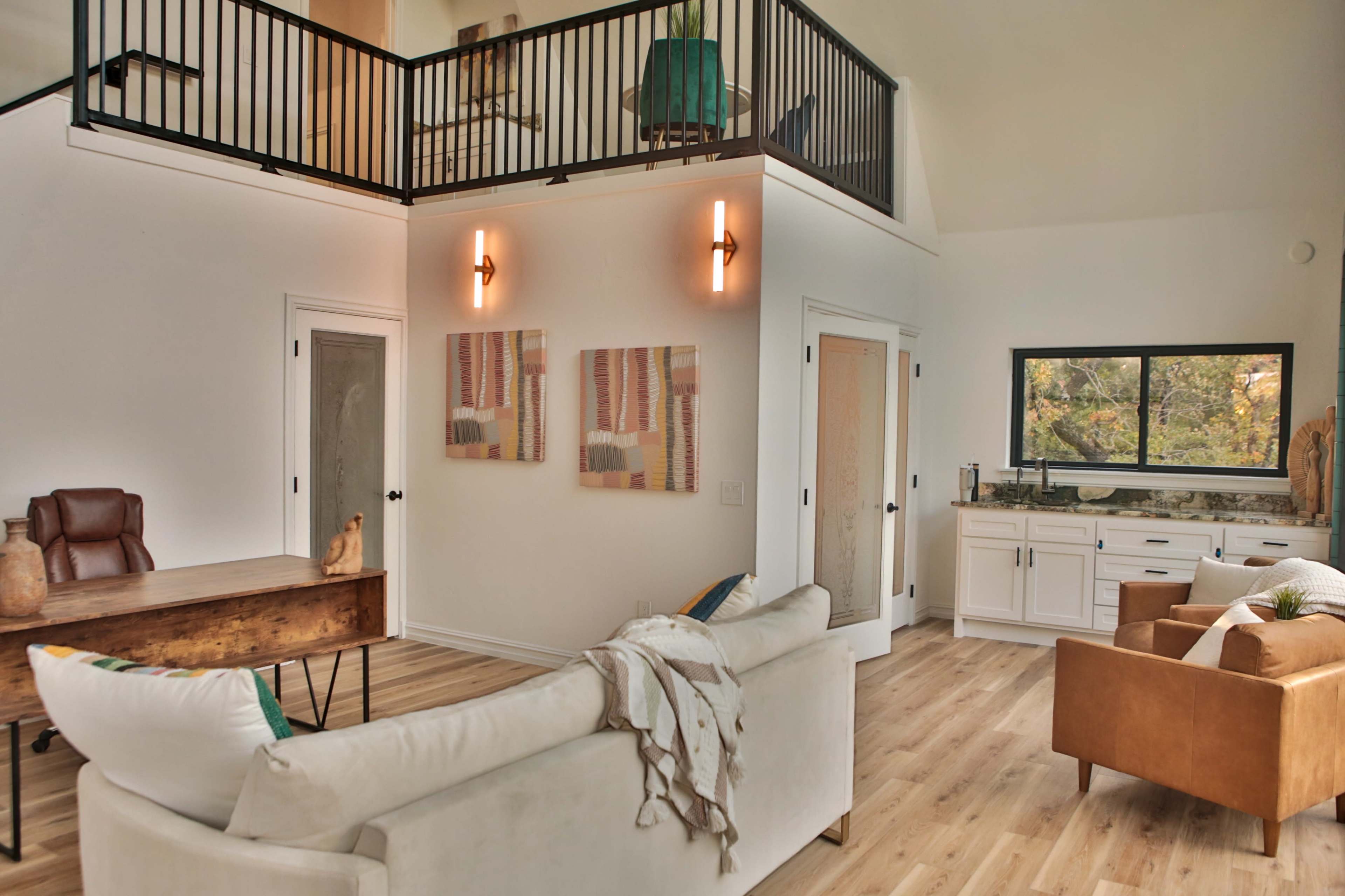 A modern living room with a high ceiling, featuring a sofa, a wooden table, and a small kitchen area.