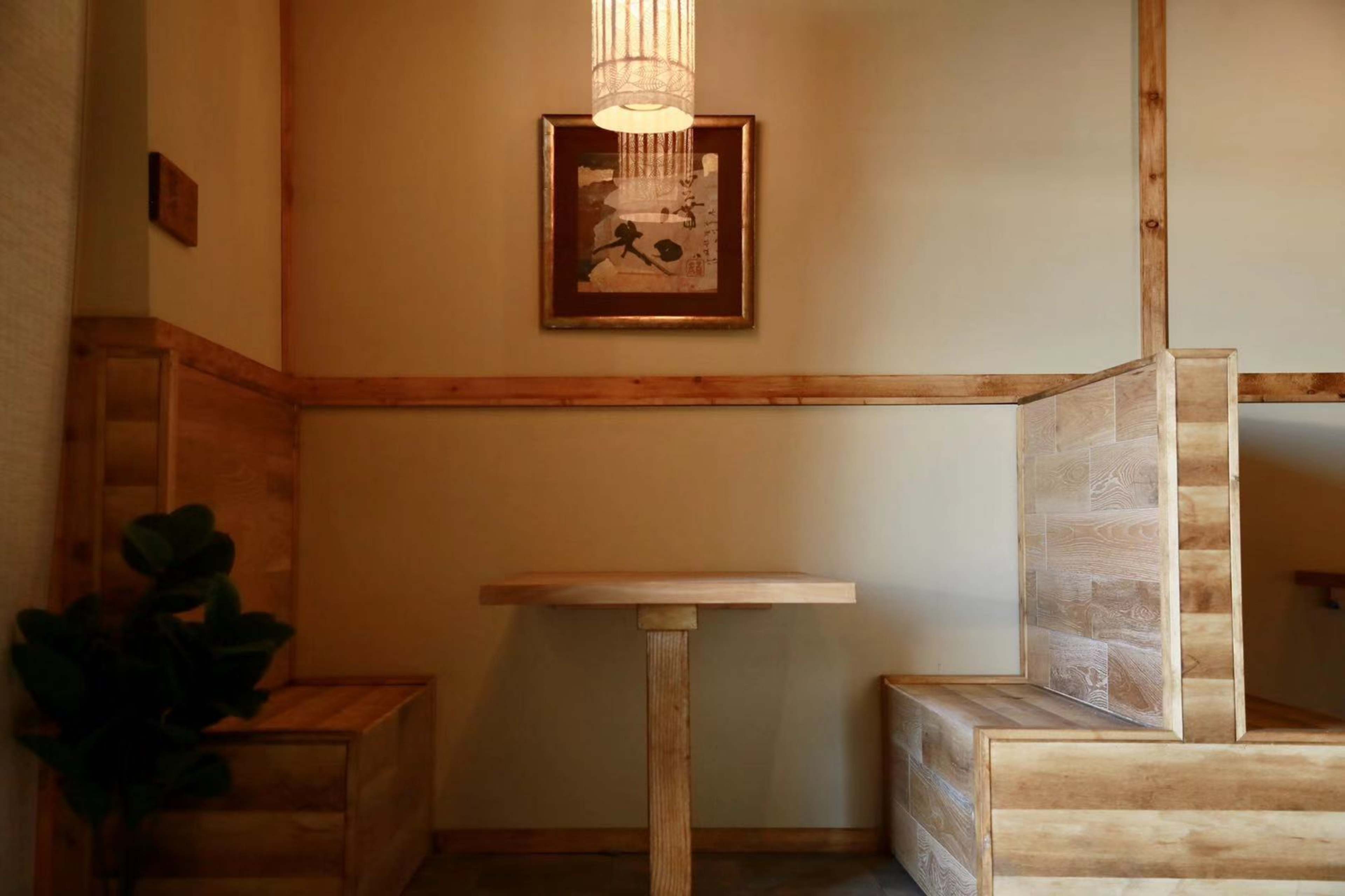 A wooden table stands in the corner of a room, flanked by two wooden benches and illuminated by a pendant light above.