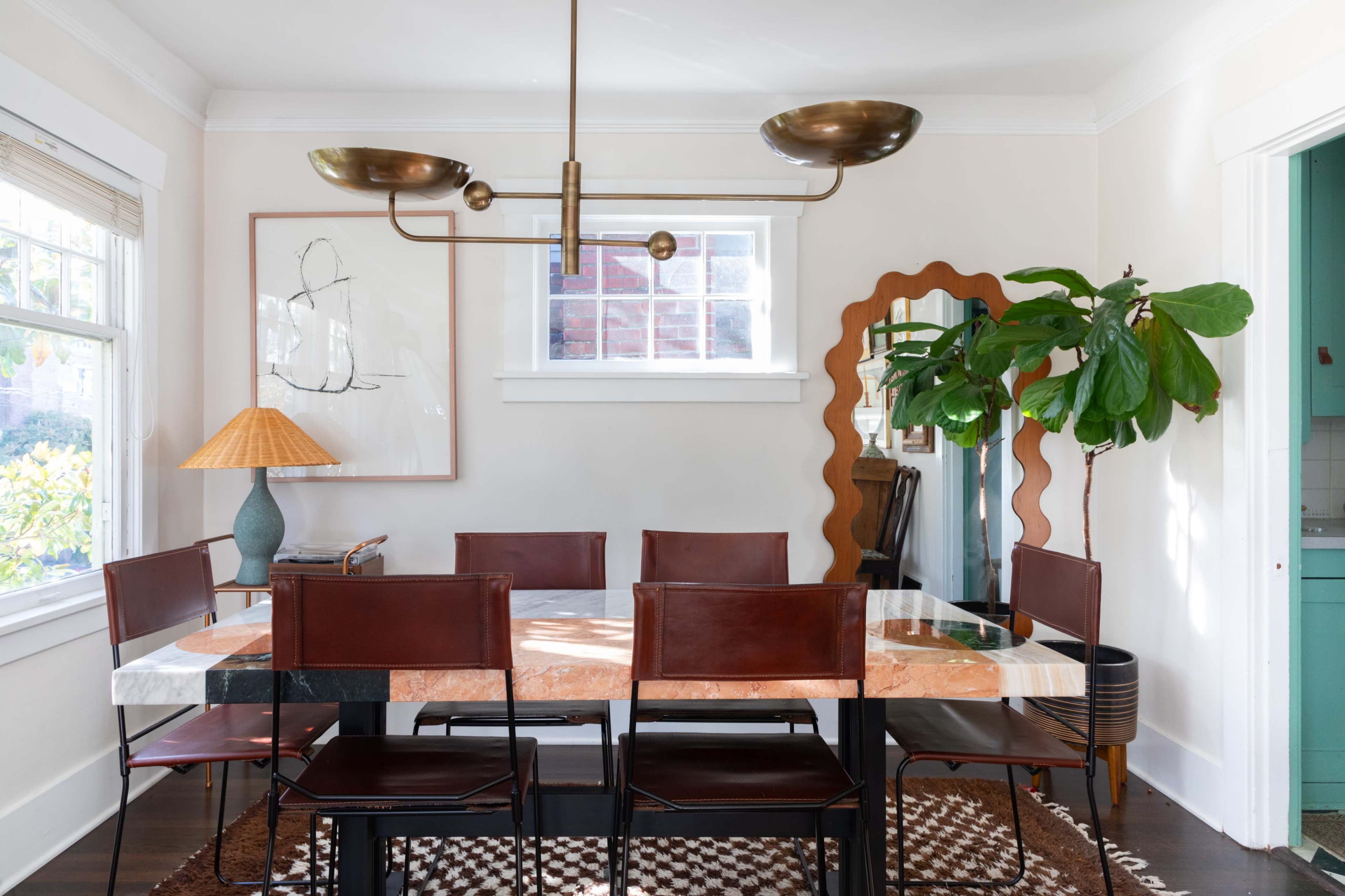 A modern dining room features a large marble-topped table surrounded by brown leather chairs, complemented by a pendant light and a potted plant.
