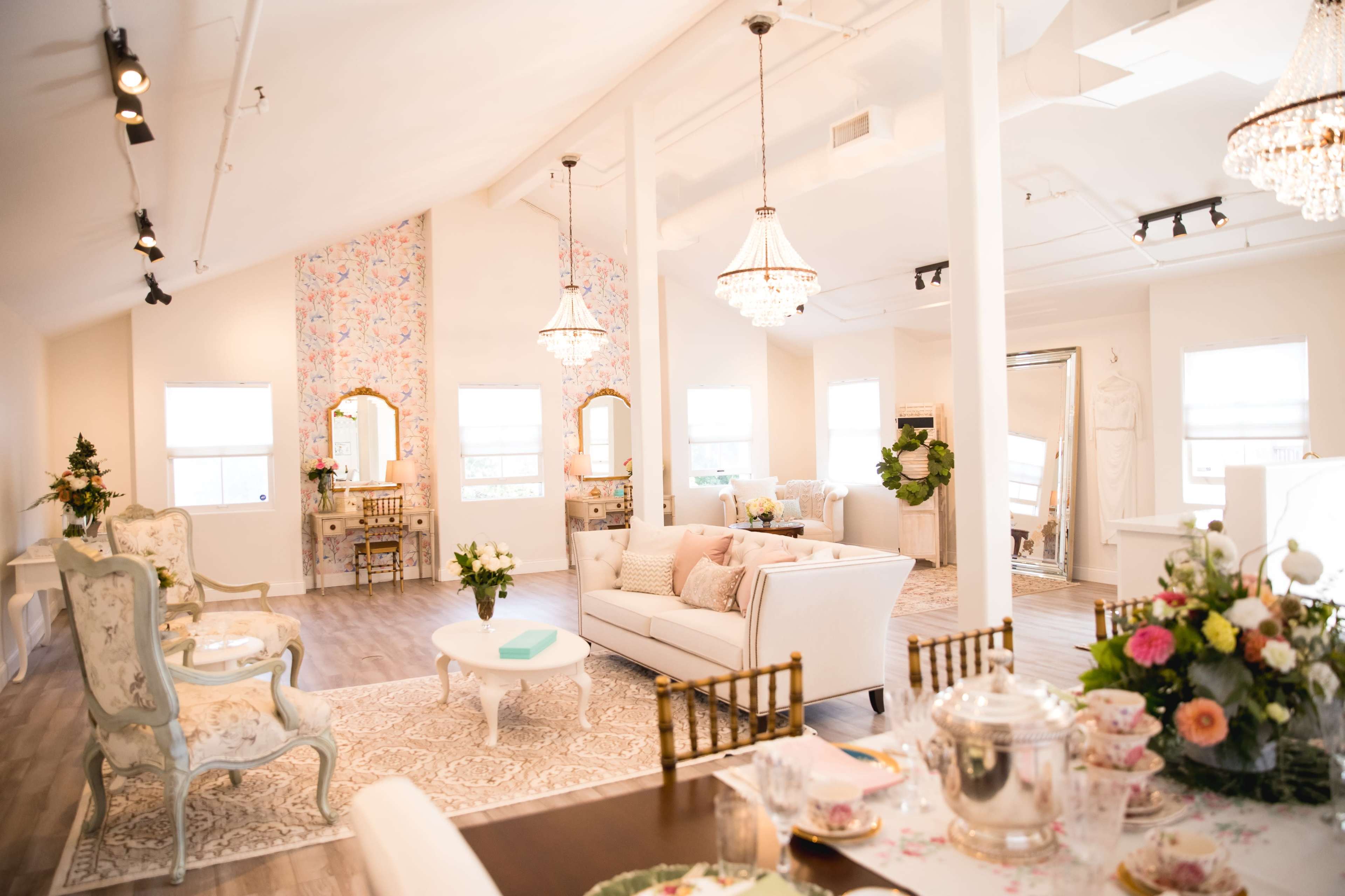 A bright, elegant interior space with vintage-style furniture, floral decor, and a dining area set for tea.