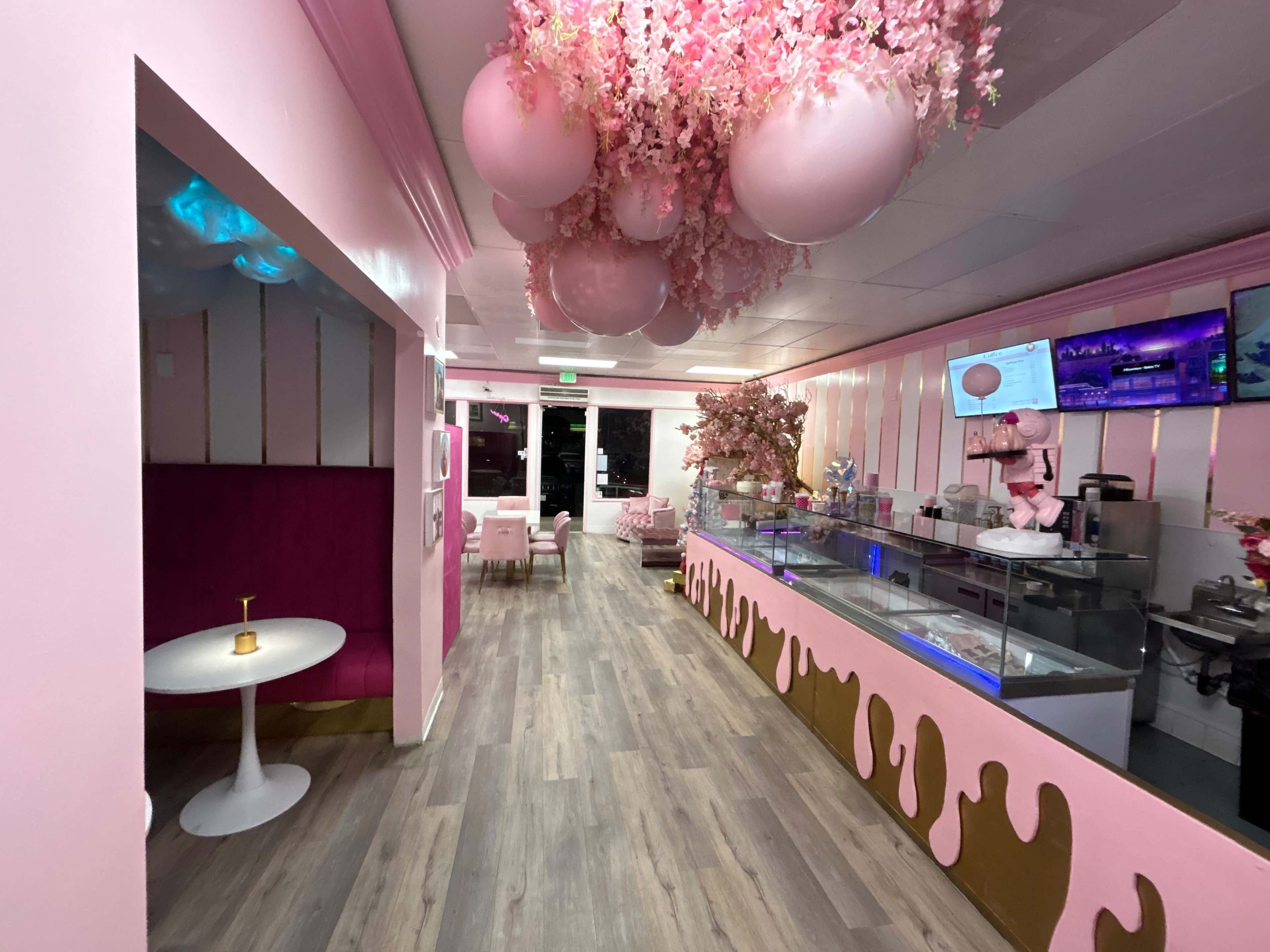 A pink-themed café interior with decorative floral arrangements and a counter displaying desserts.