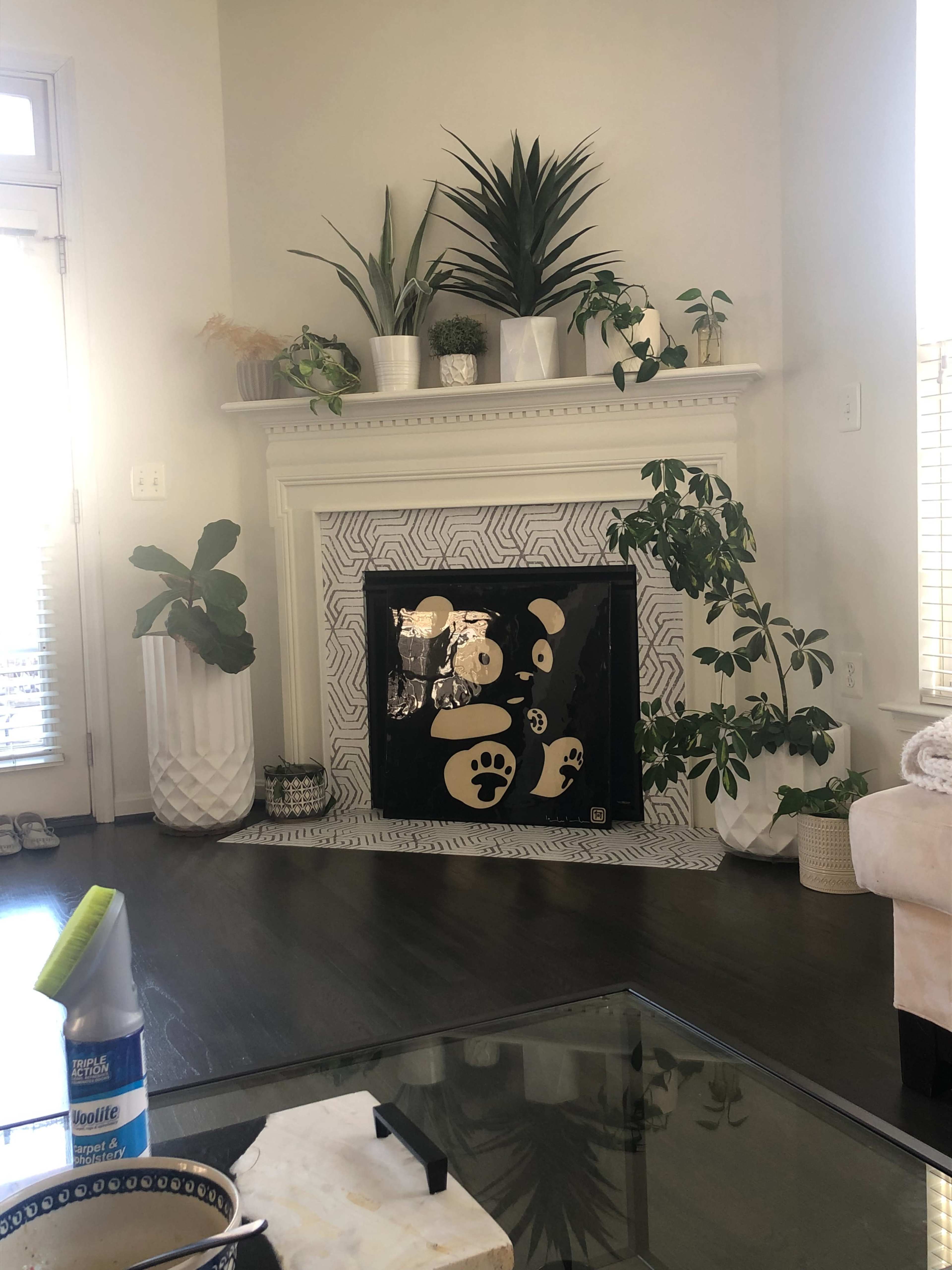 The image shows a modern living room with a decorative fireplace adorned with plants and a patterned screen featuring bear paw prints.