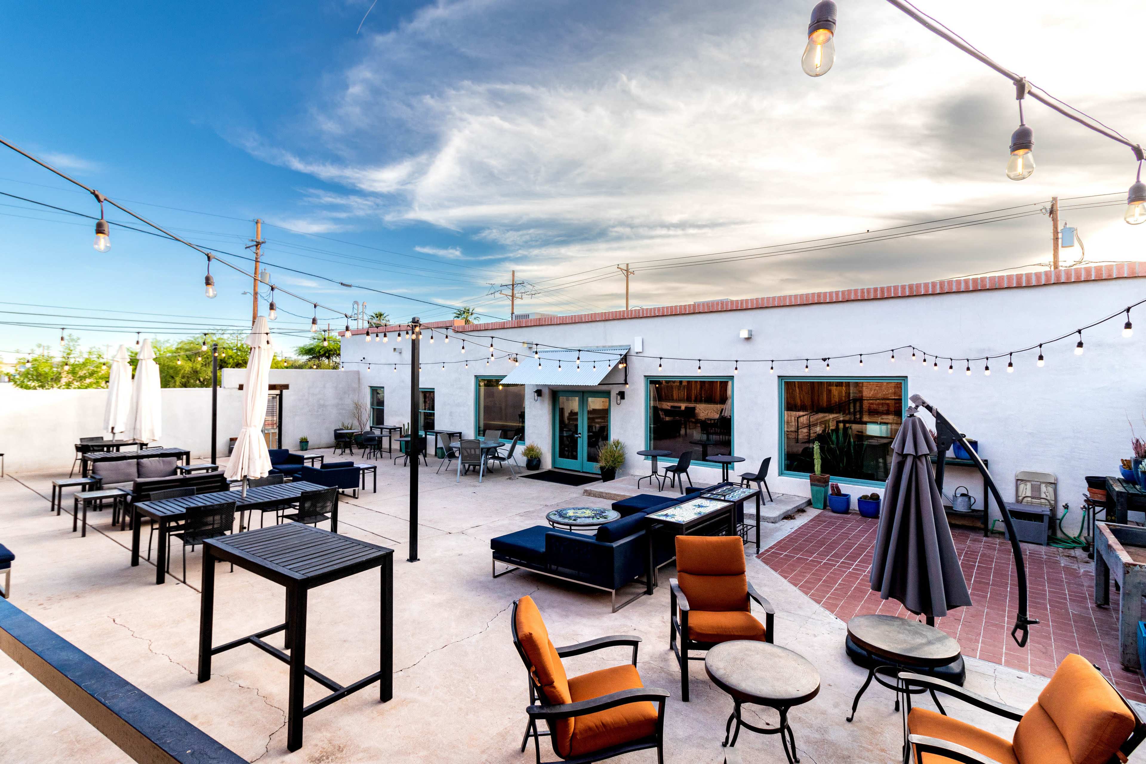 An outdoor patio area with tables and chairs, string lights, and several umbrellas under a clear blue sky.