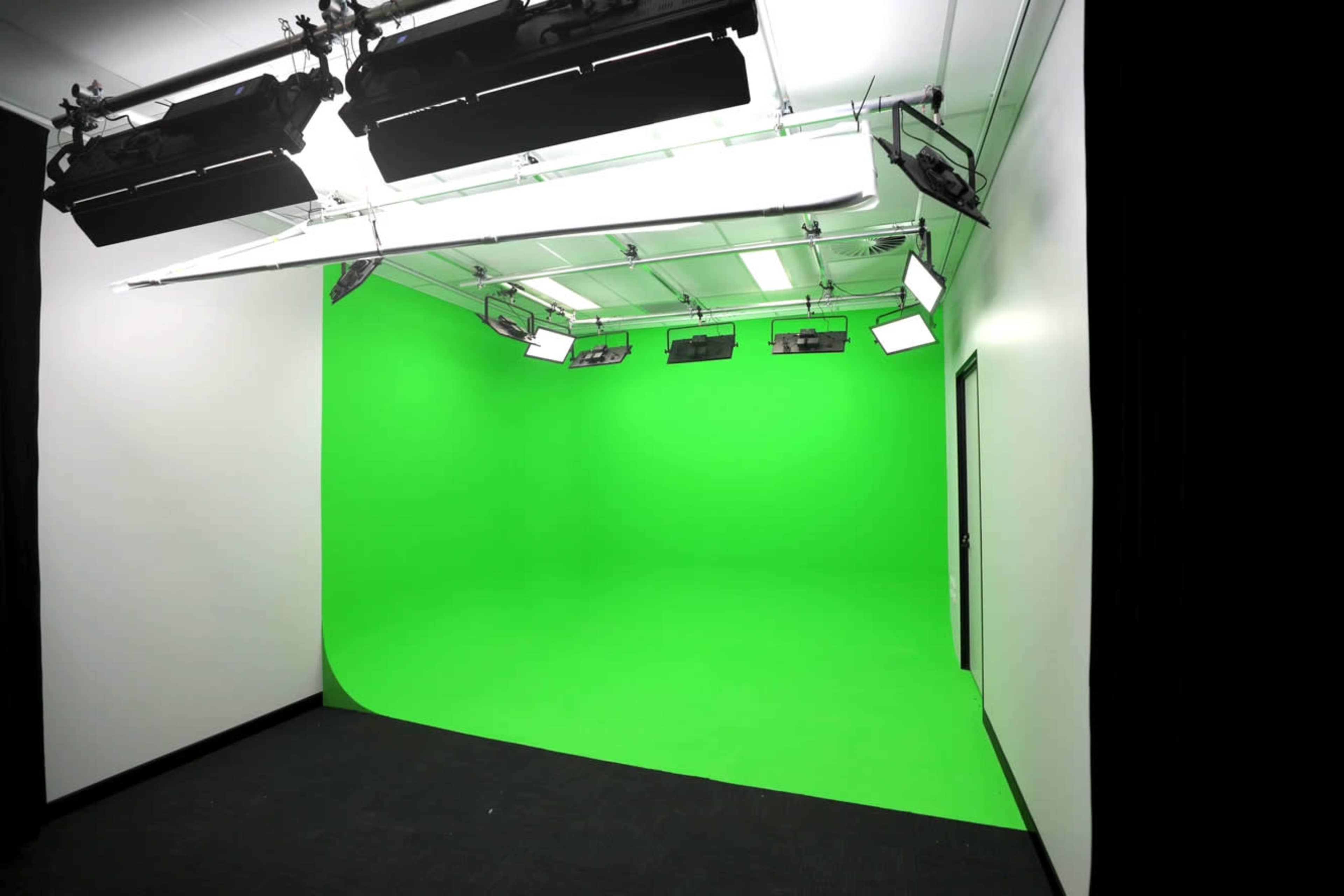 The image shows a green screen studio with bright lights and a seamless green backdrop.