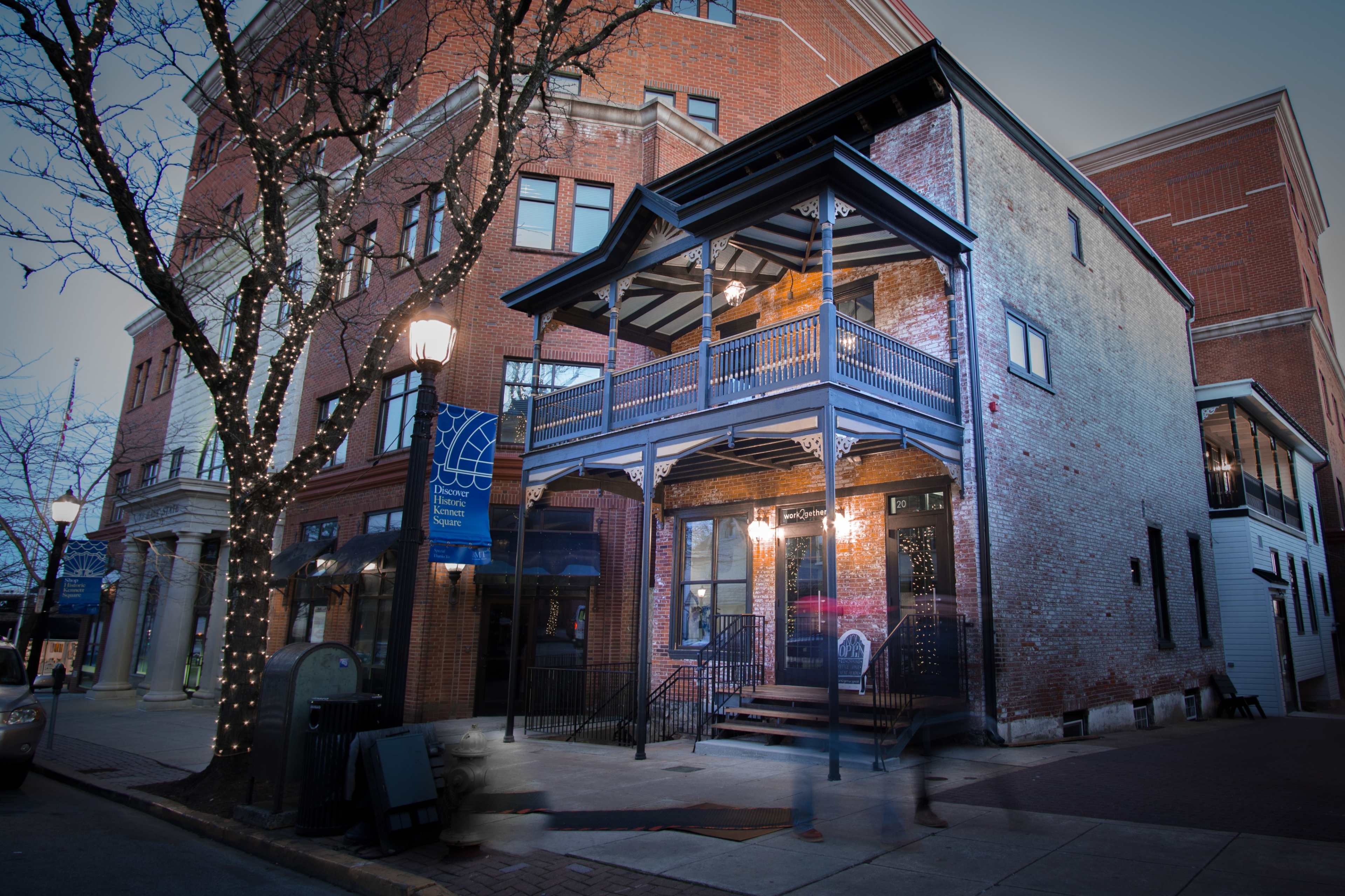 A historic brick building with a two-story balcony is illuminated by street lamps in a bustling urban area.