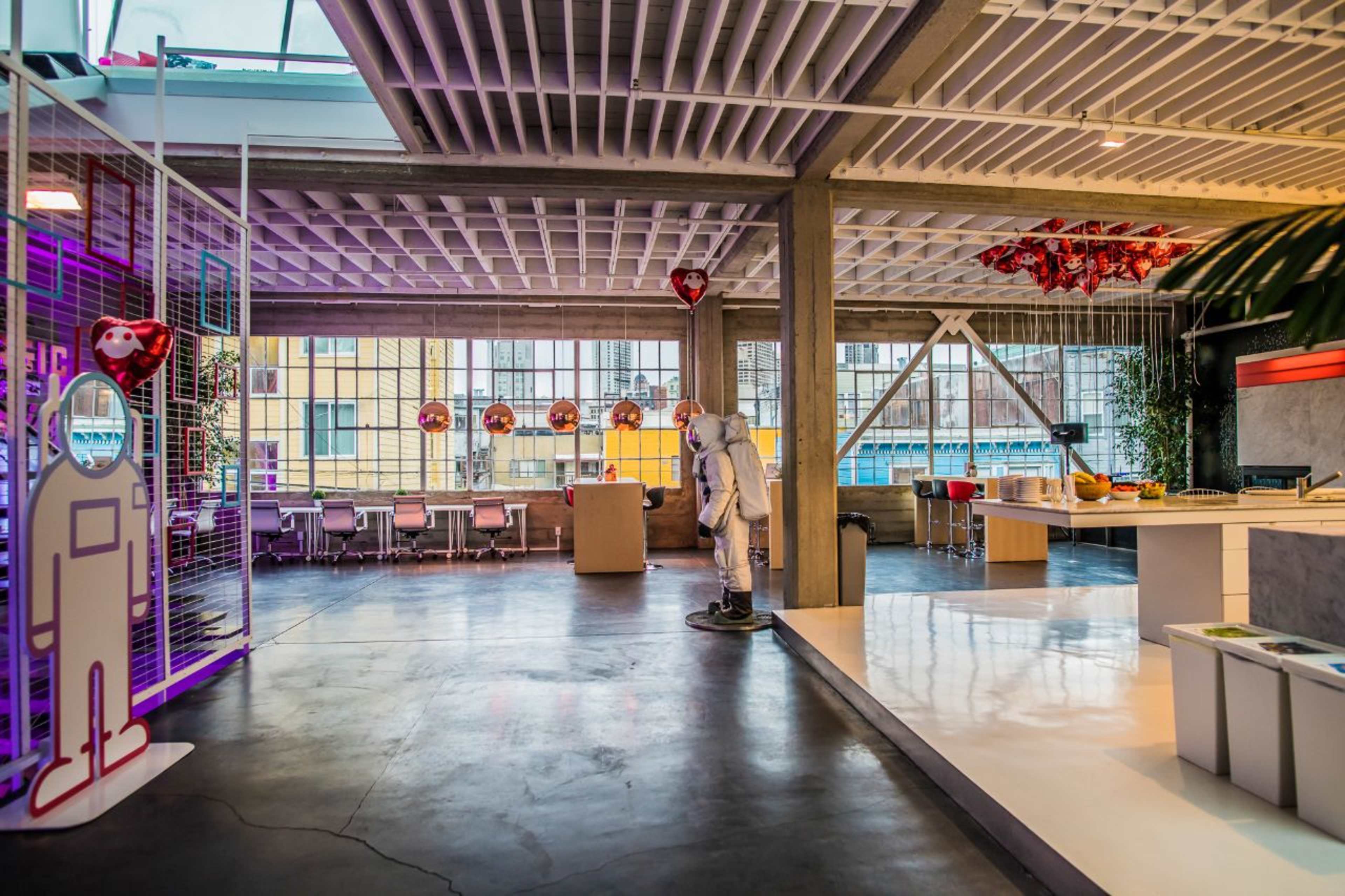 A modern office space with large windows, colorful decorations, and an astronaut figure standing in the foreground.