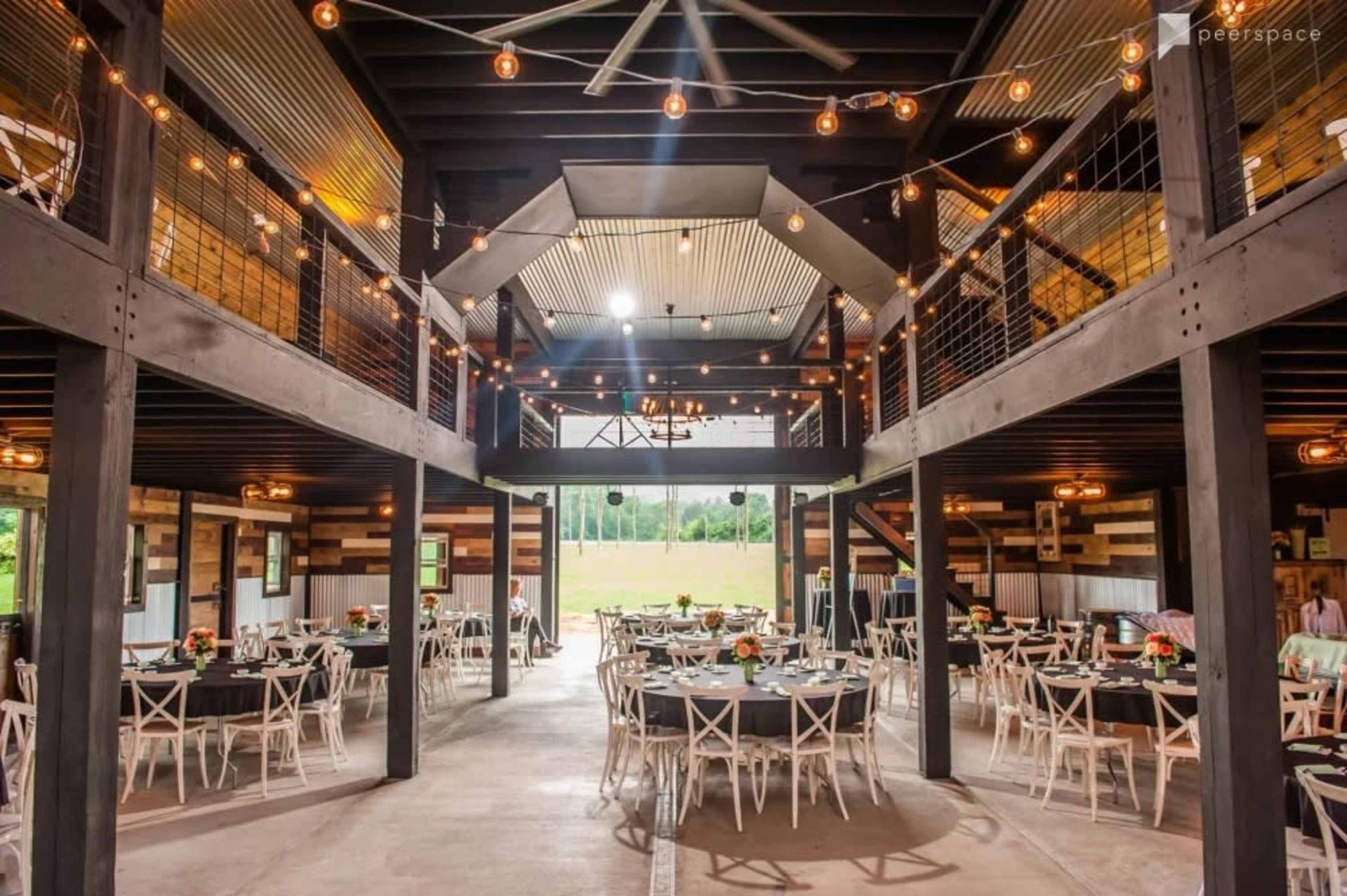 A spacious event venue with round tables set for dining, string lights overhead, and a two-level design featuring an open layout.