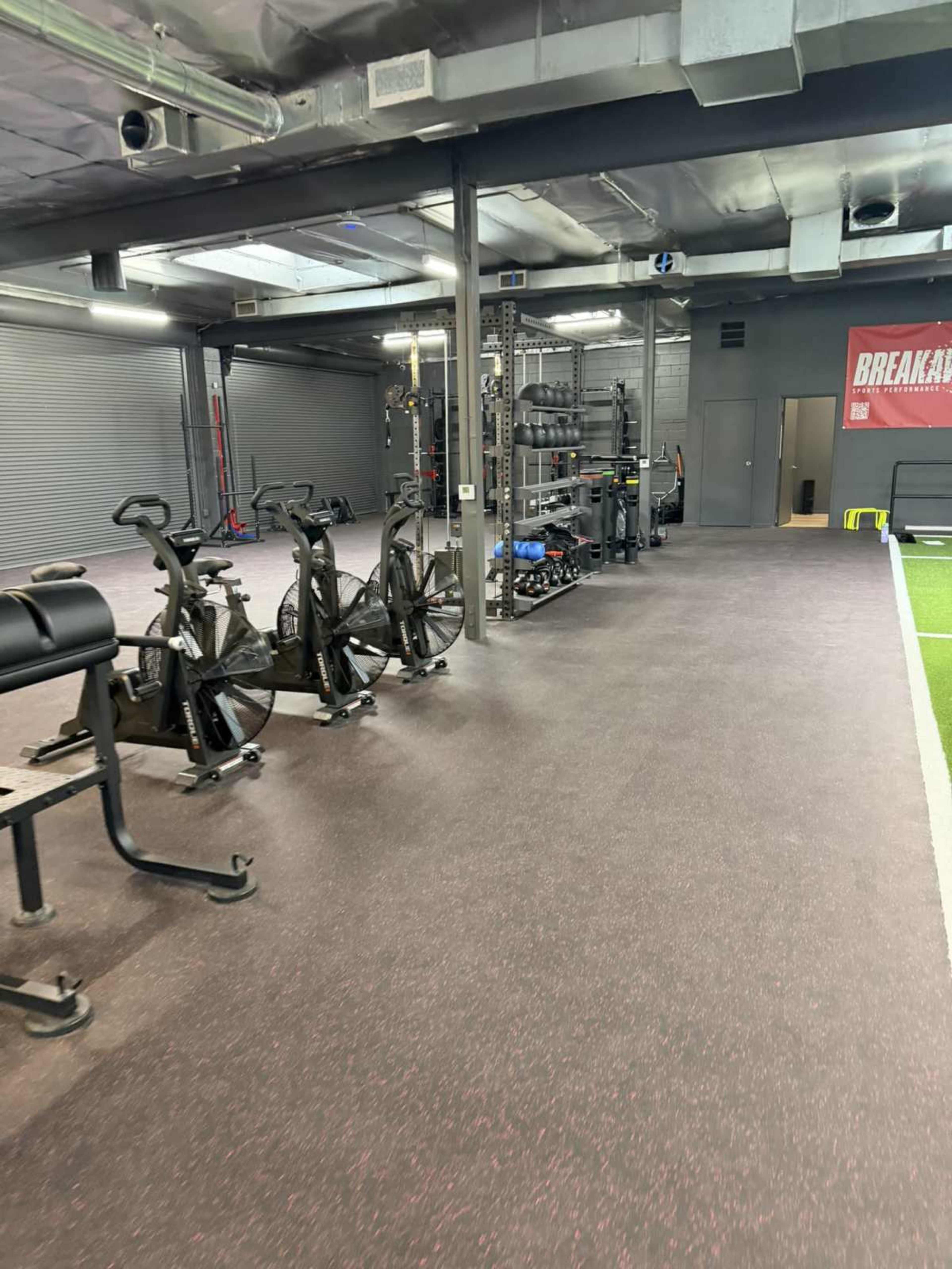 The image shows a modern gym with exercise equipment, including stationary bikes and weightlifting stations, set against a grey interior.