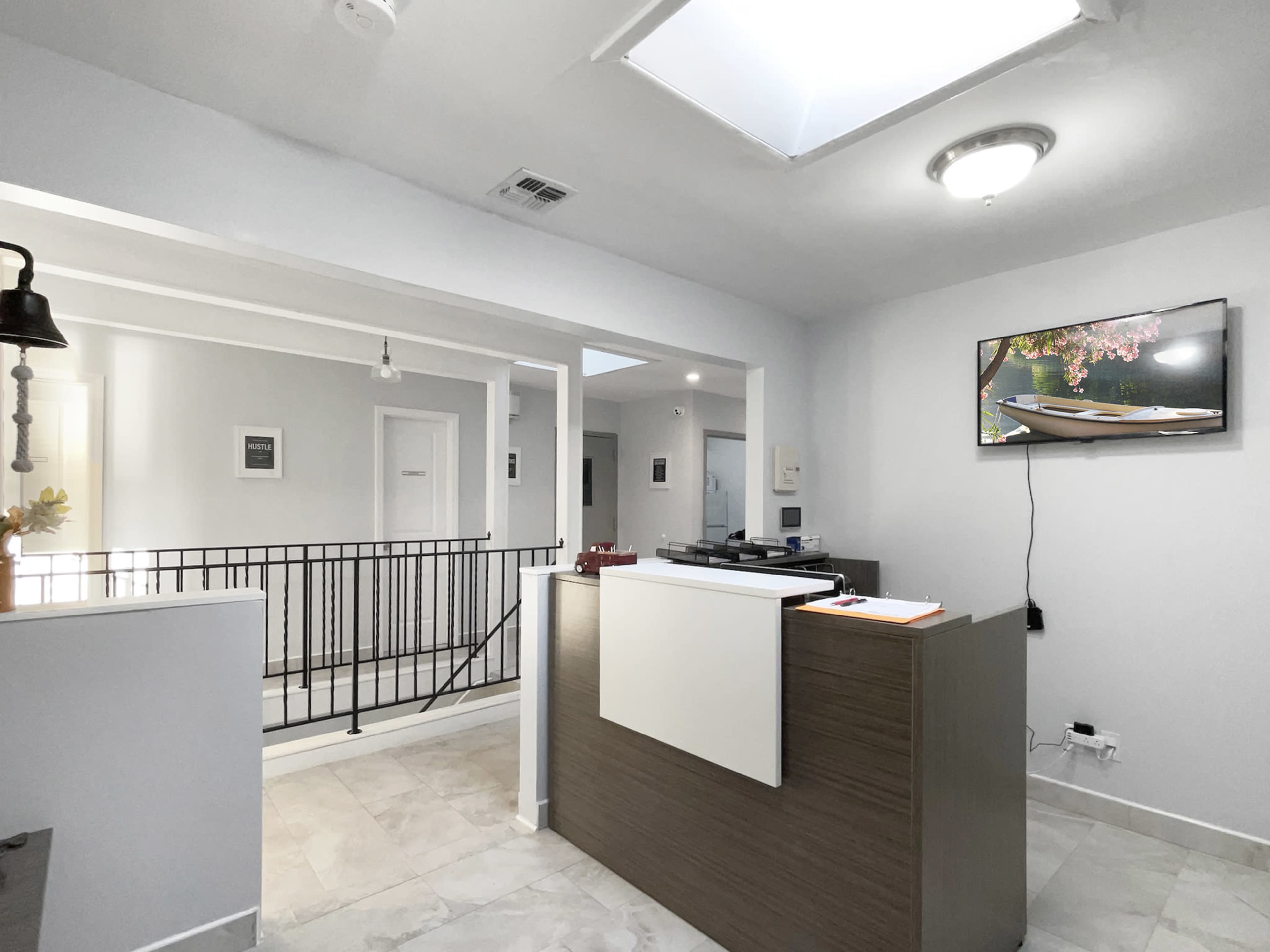 A modern reception area with a wooden front desk, a skylight, and a wall-mounted television displaying an image of a boat.
