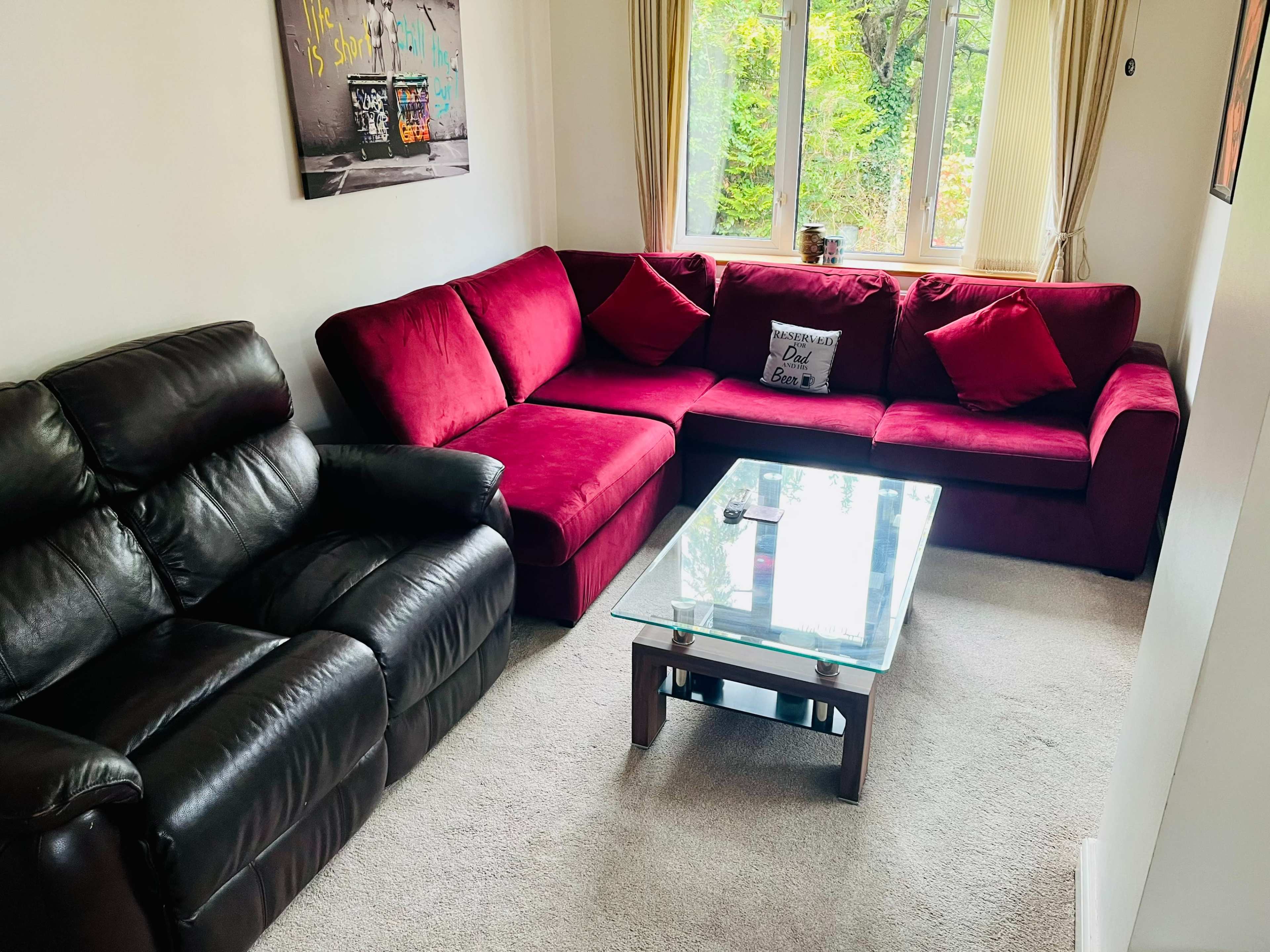 A living room with a red sectional sofa, a black leather recliner, and a glass coffee table on a carpeted floor.