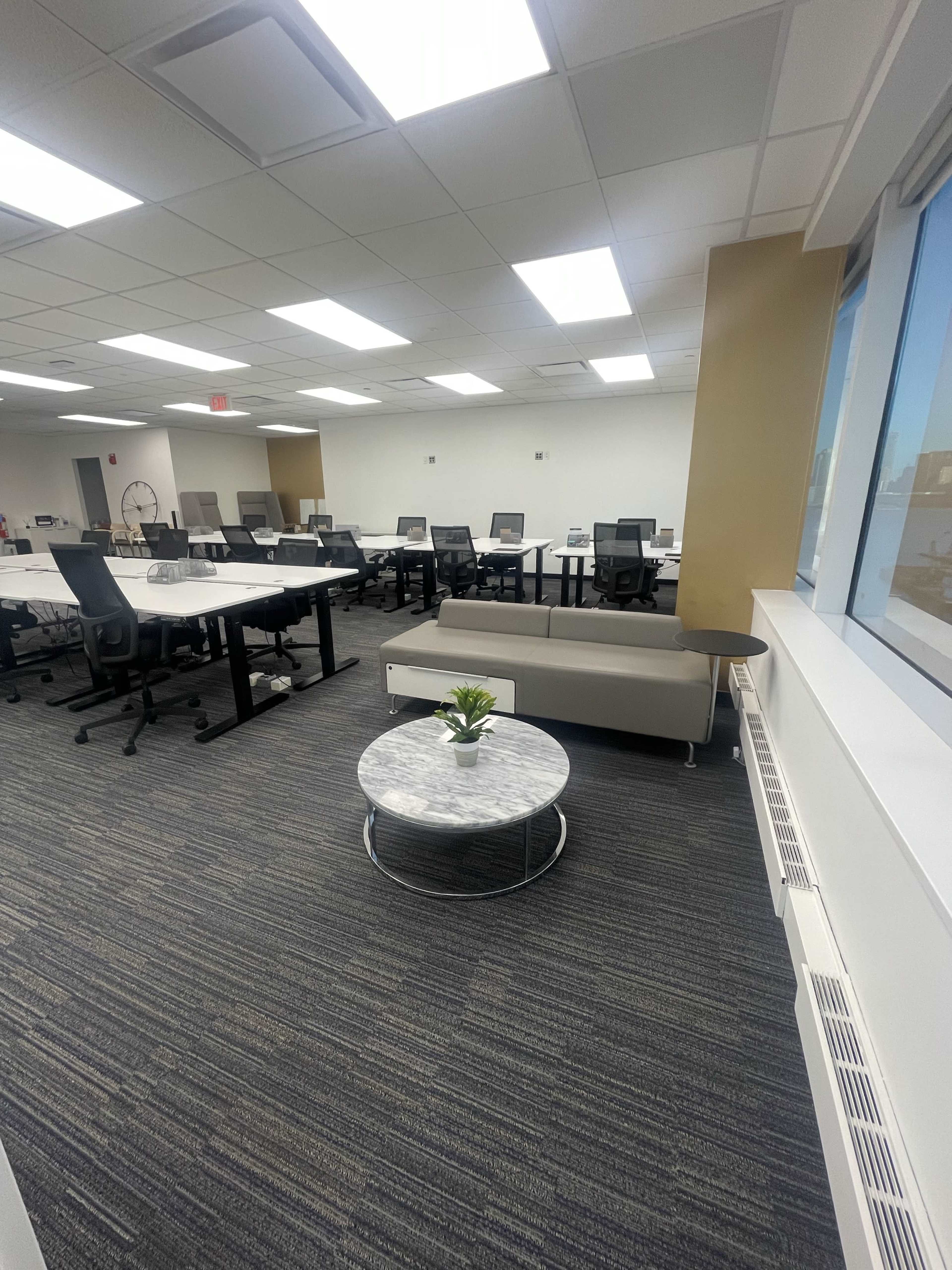 A modern office space with several workstations, a circular coffee table, and a sofa near a window.