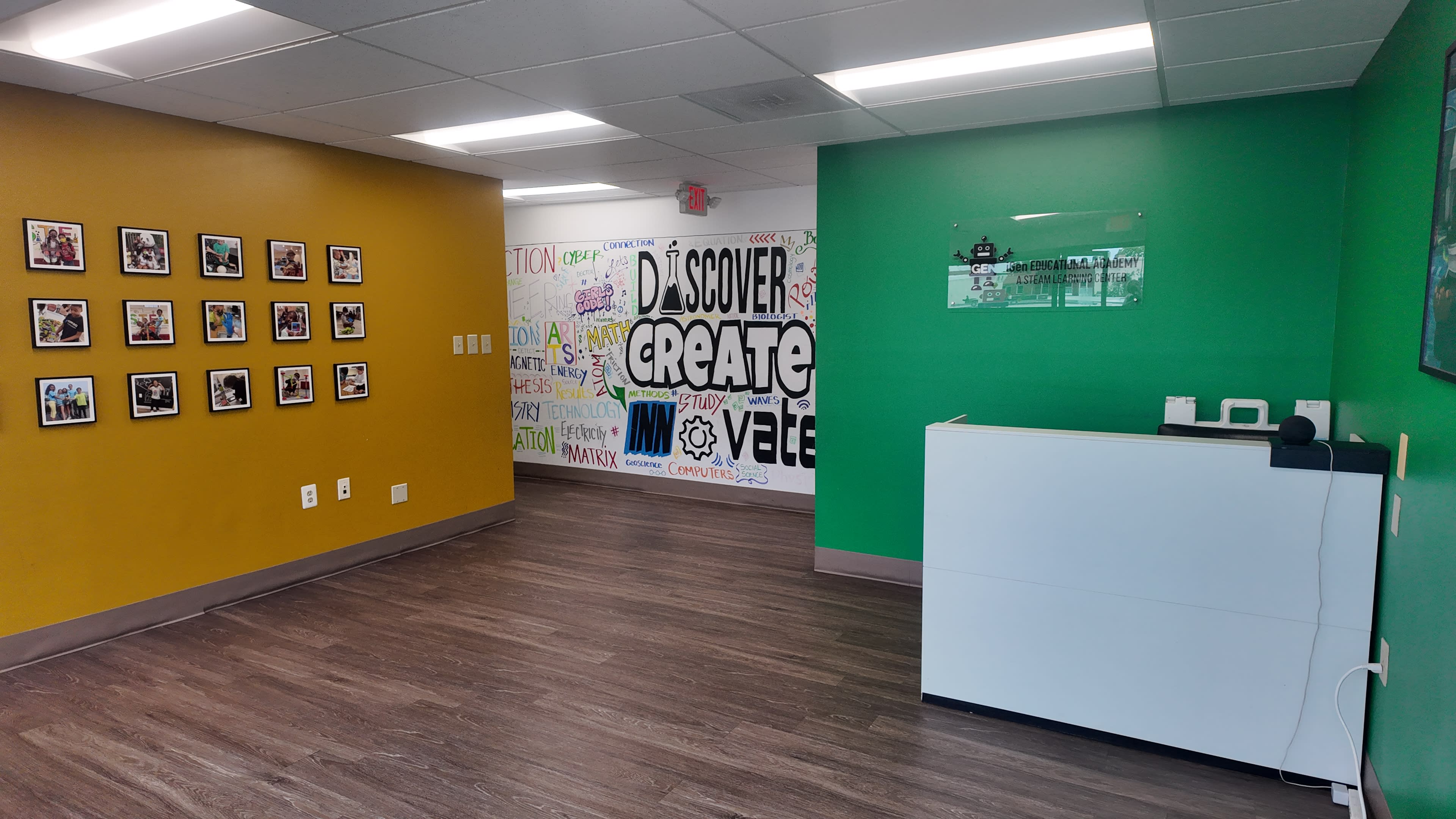The image shows a modern office space with a green and yellow accent wall, framed photos on one side, and a white reception desk in the foreground.