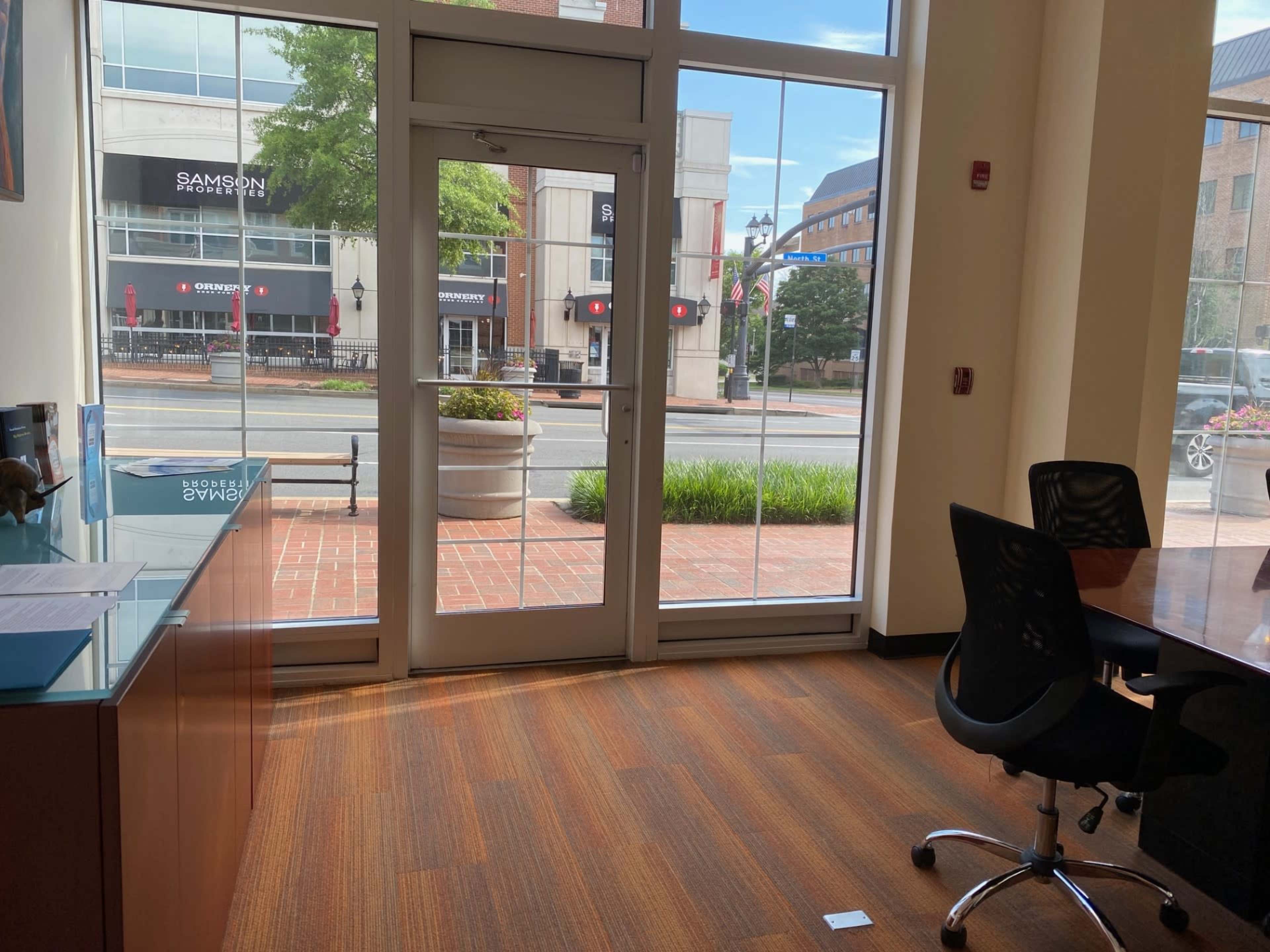 The image shows an office interior with a glass entrance facing a well-lit street, featuring a desk and chairs.