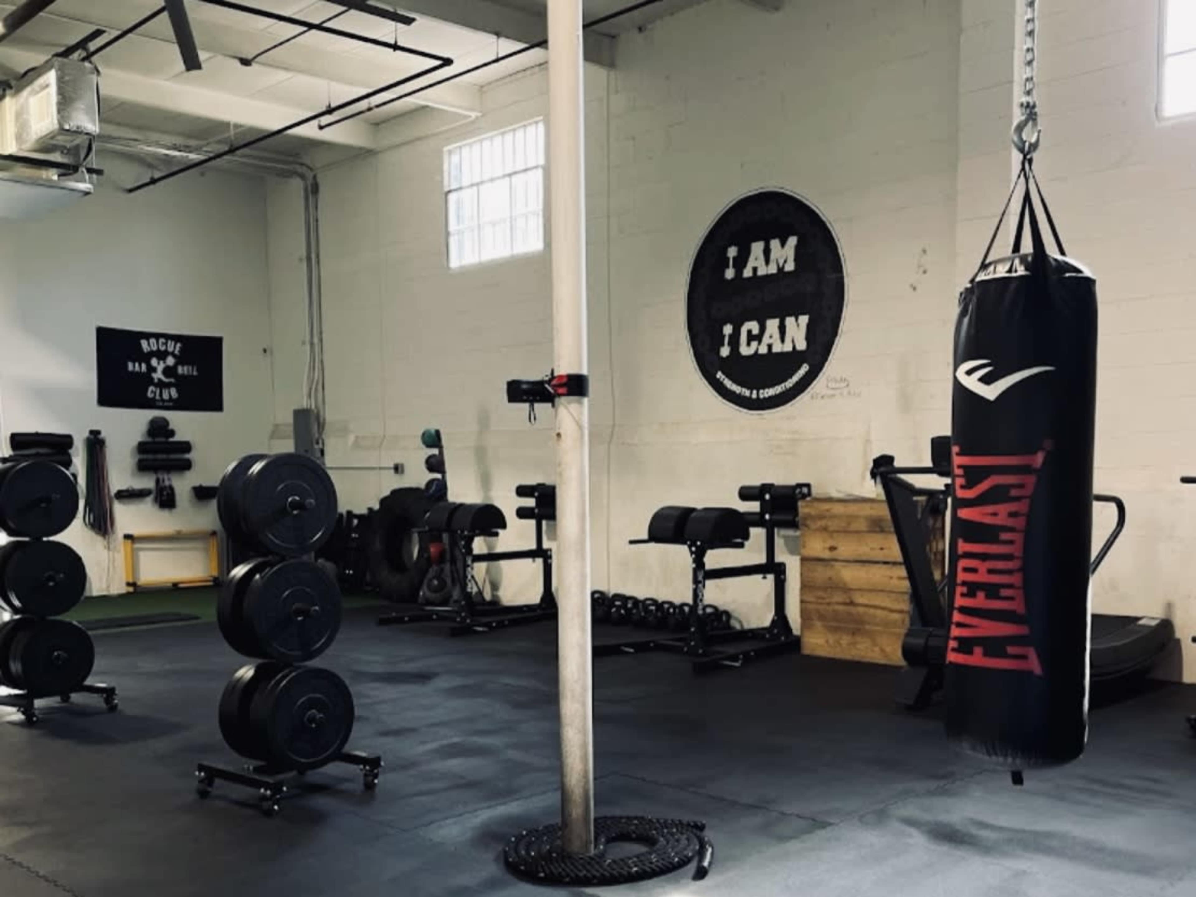 An industrial-style gym with a punching bag, free weights, and various exercise equipment arranged around a central pole.