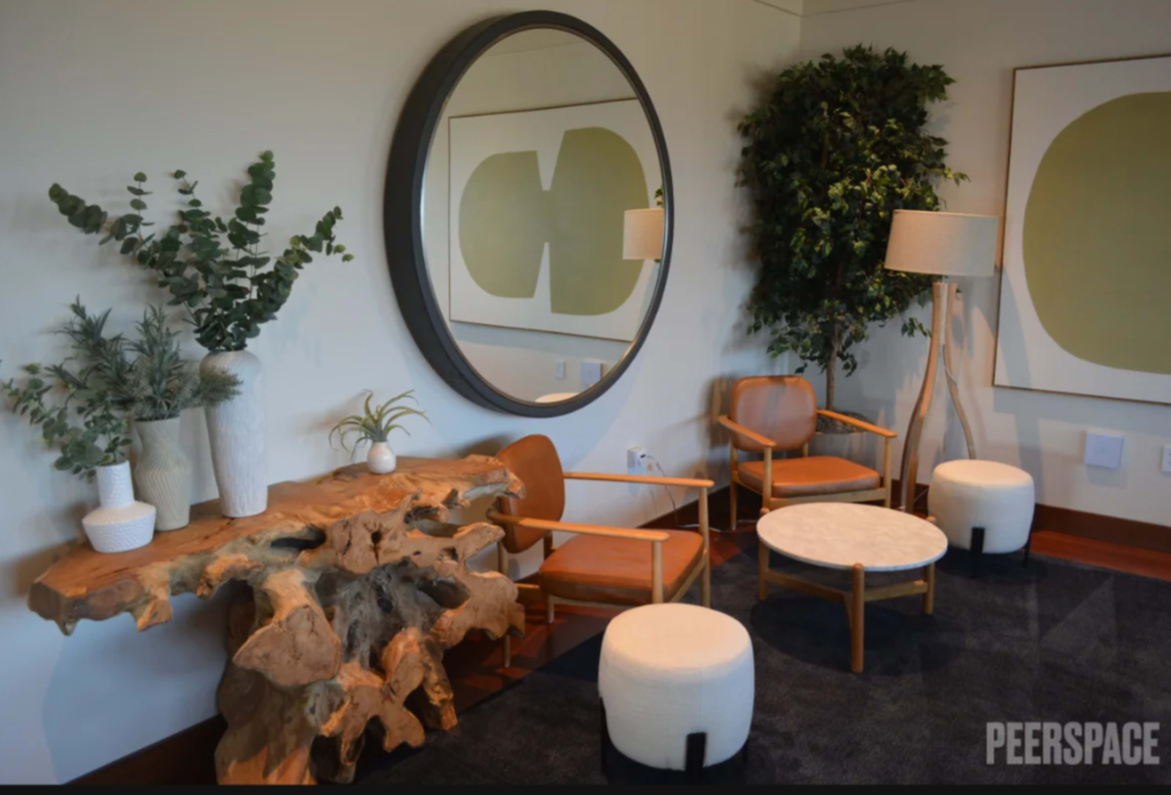 The image depicts a cozy seating area featuring two wooden chairs, a circular mirror, a decorative wooden table, and a potted plant.