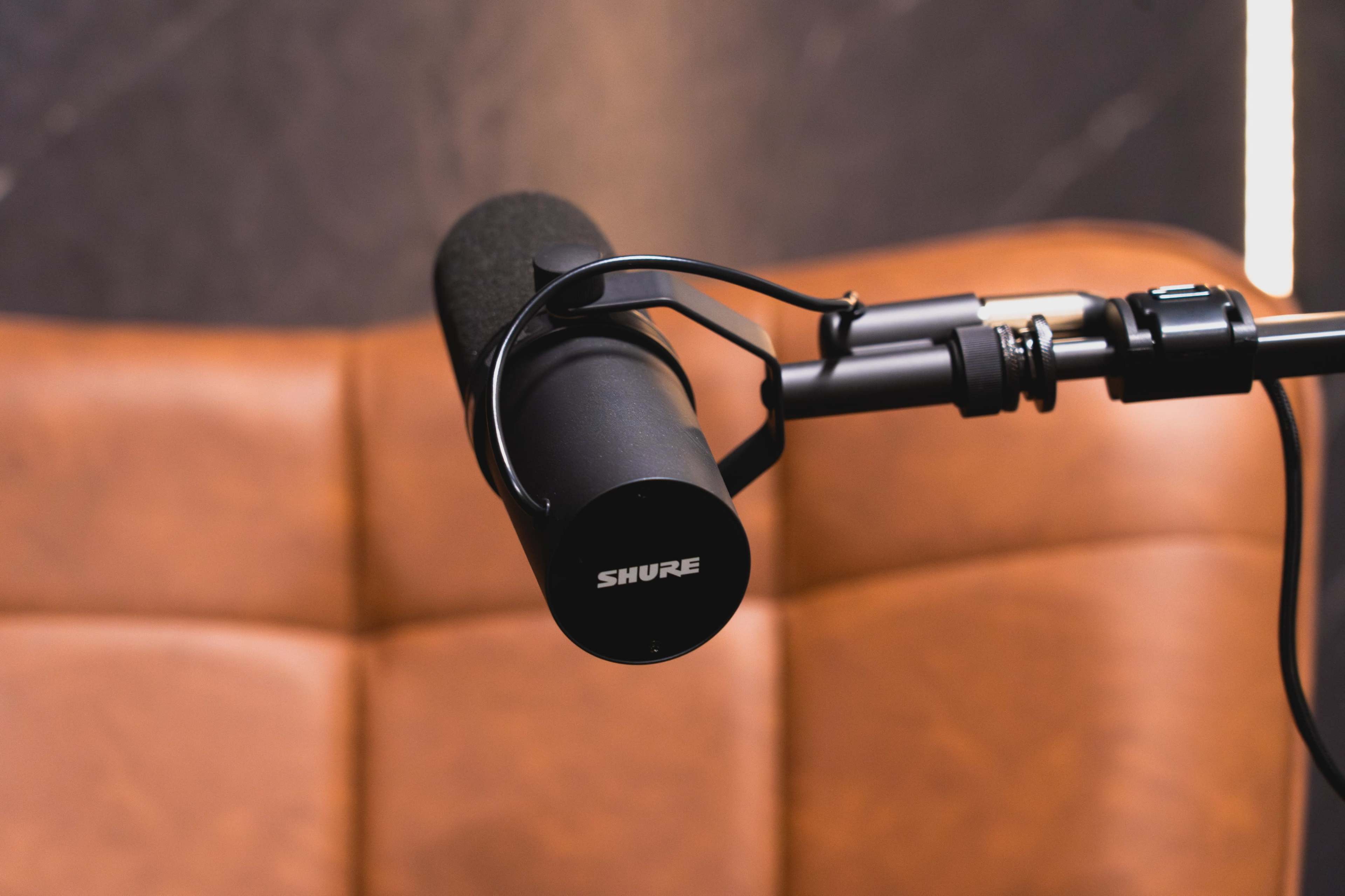 A black Shure microphone is mounted on a mic stand in front of a brown leather background.