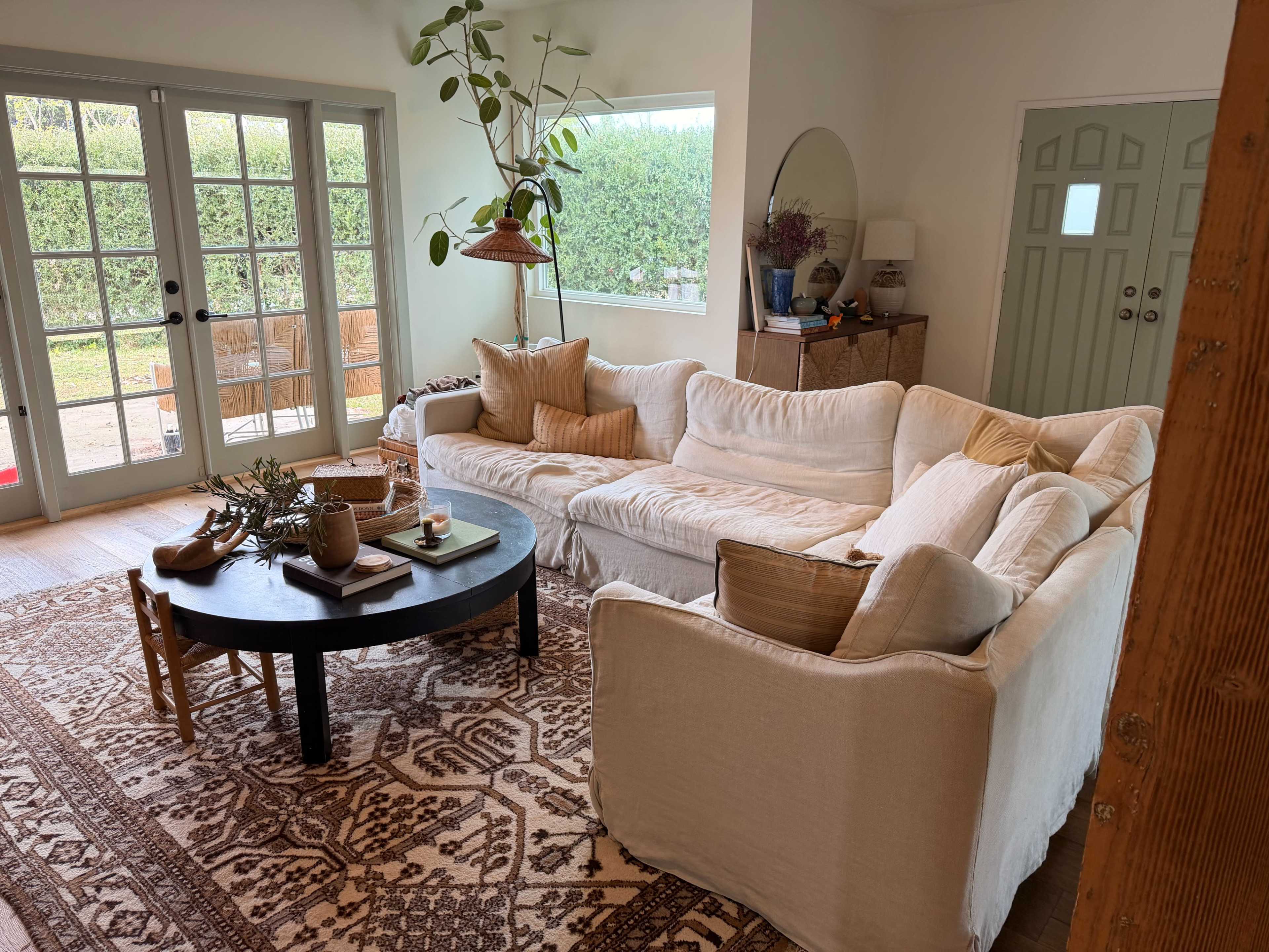 The living room features a white sectional sofa, a round black coffee table, and large glass doors opening to a garden.