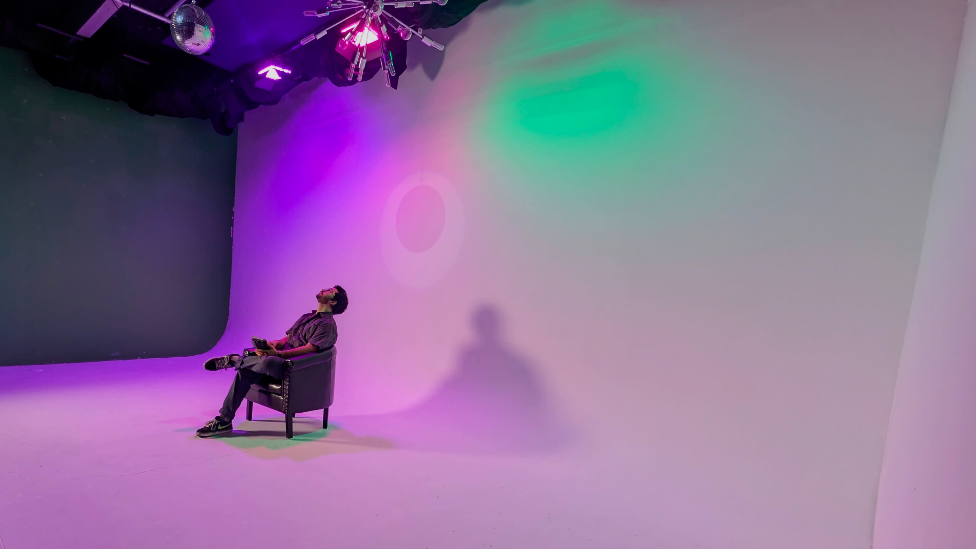 A person sits in a chair, gazing upwards under colorful lights in a studio setting.