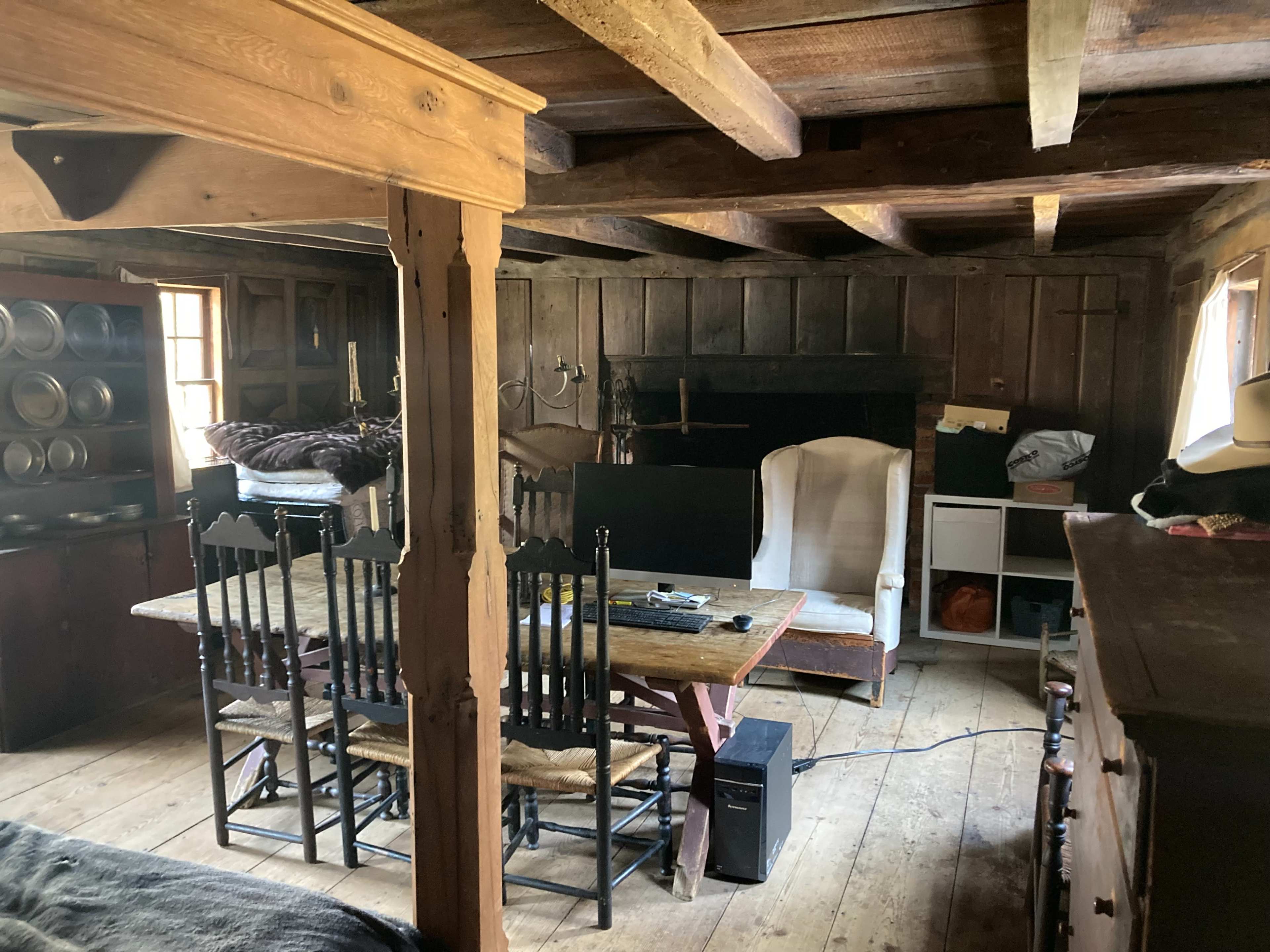 A rustic interior of a wooden room featuring a dining table with chairs, a white armchair, and a dark wooden cabinet.