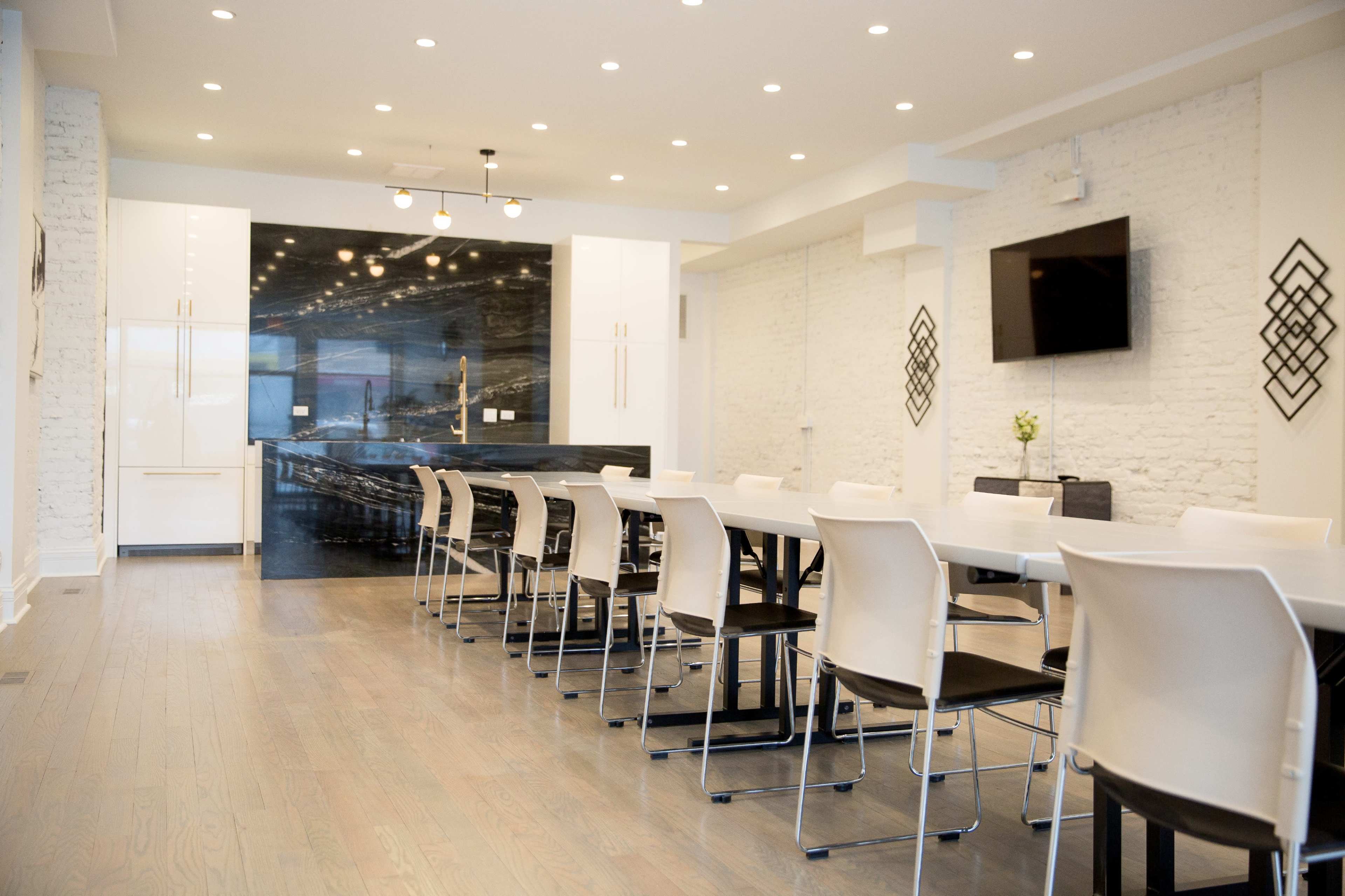 A modern conference room features a long white table surrounded by chairs, with a sleek black wall and a television at the far end.