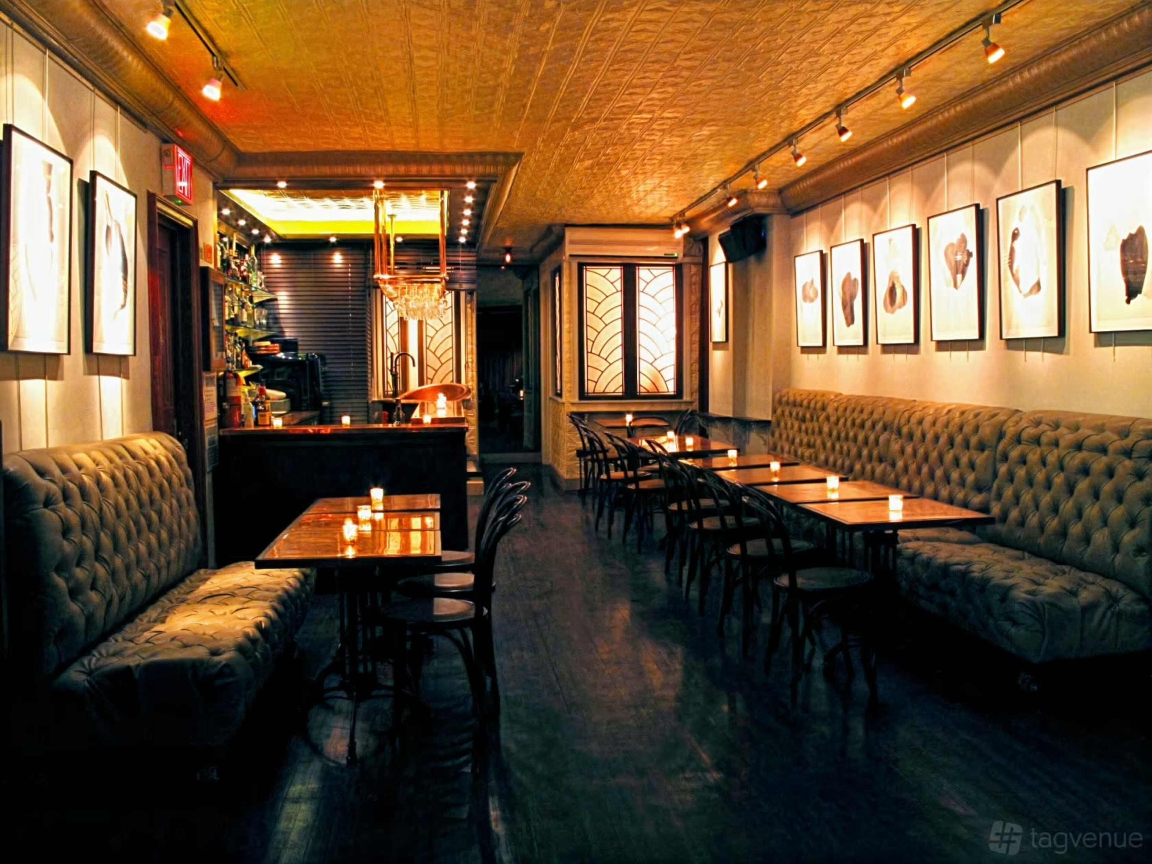 The image shows a dimly lit restaurant interior with tufted seating arrangements, wooden tables, and framed artwork on the walls.