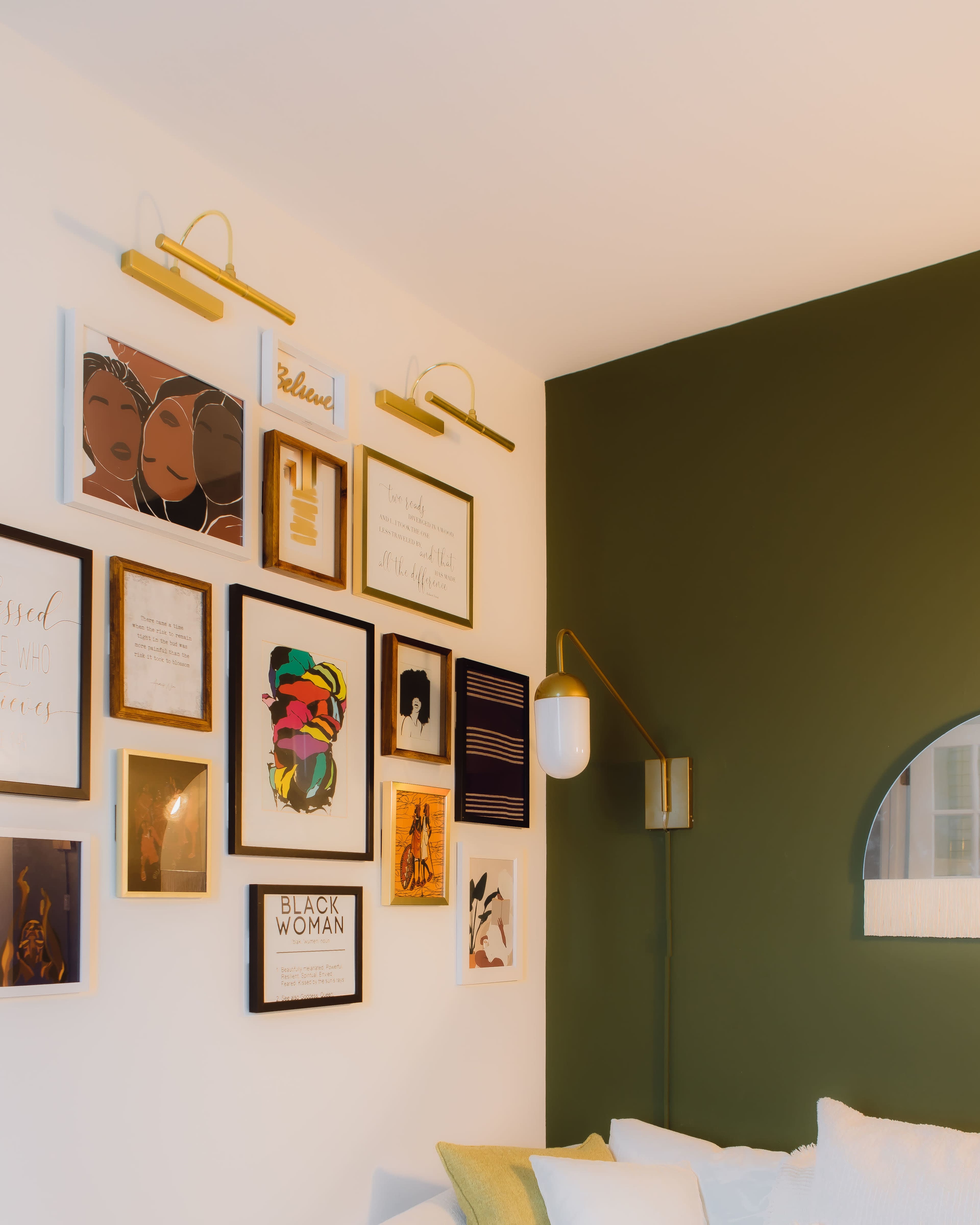 The image depicts a modern living room corner featuring a gallery wall of framed art and photographs in various styles, along with a green accent wall and a lamp.
