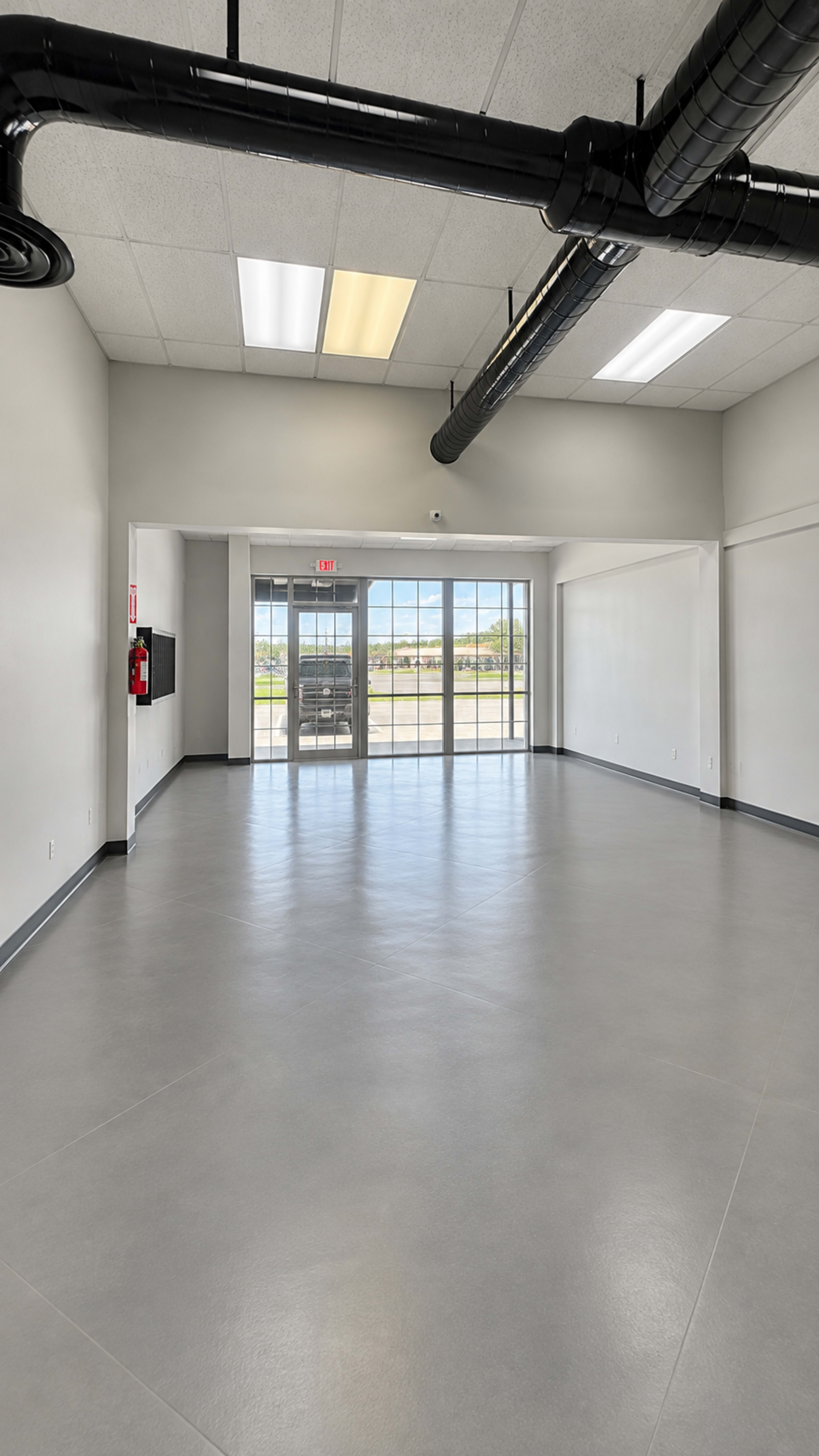 The image shows a spacious, empty commercial interior with large windows and a modern ceiling design.