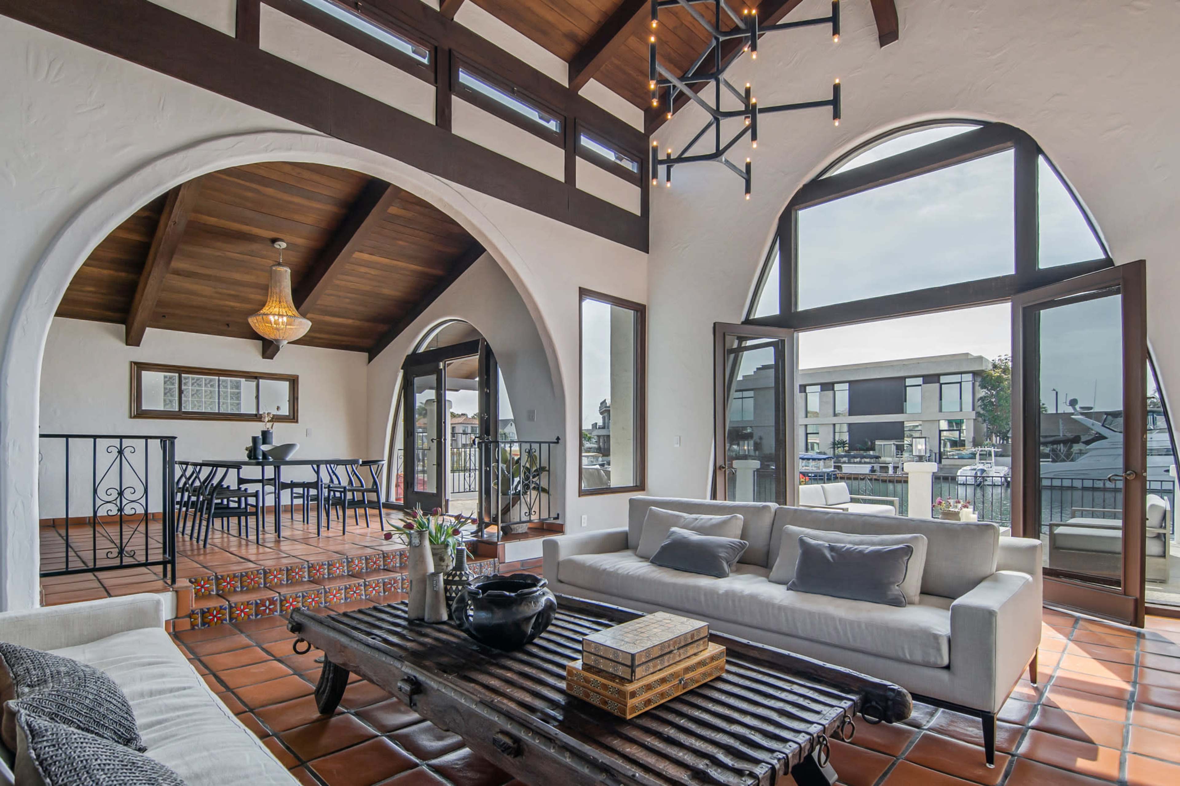 A spacious living room features large arched windows, a wooden ceiling, and a mix of modern and traditional furnishings.