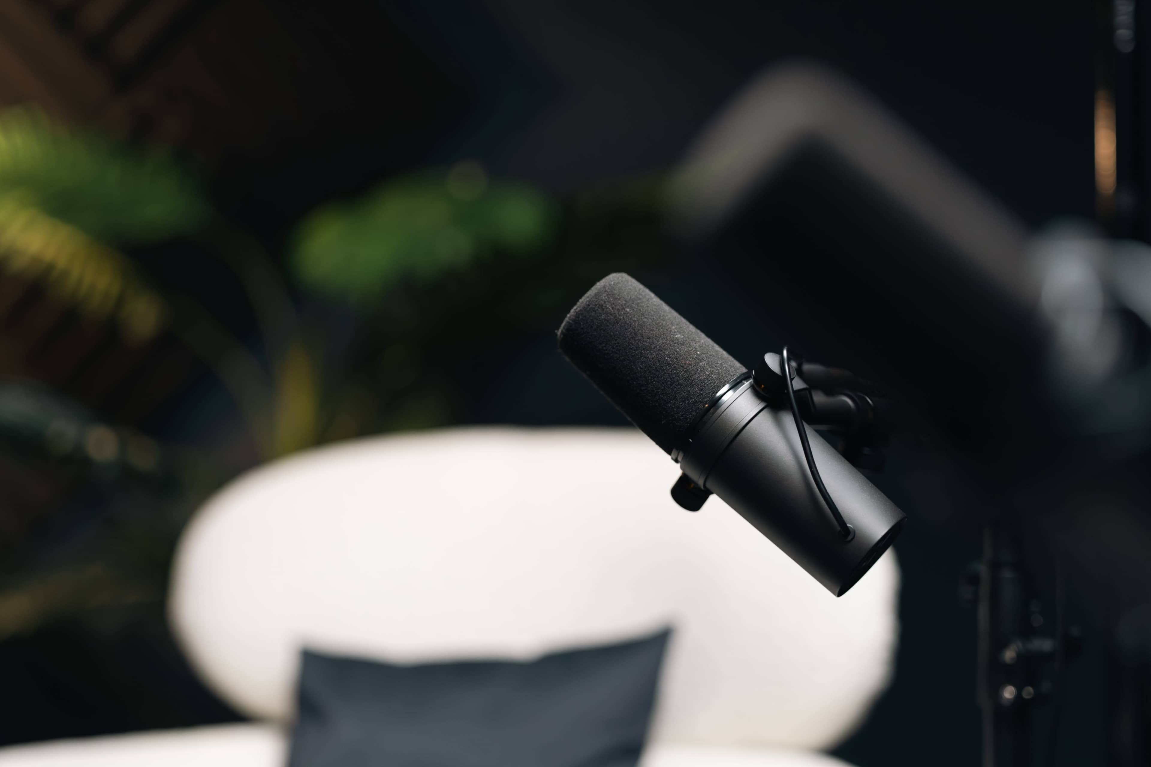 A close-up of a black microphone positioned near a softly lit background with a plush, white chair and a dark cushion.