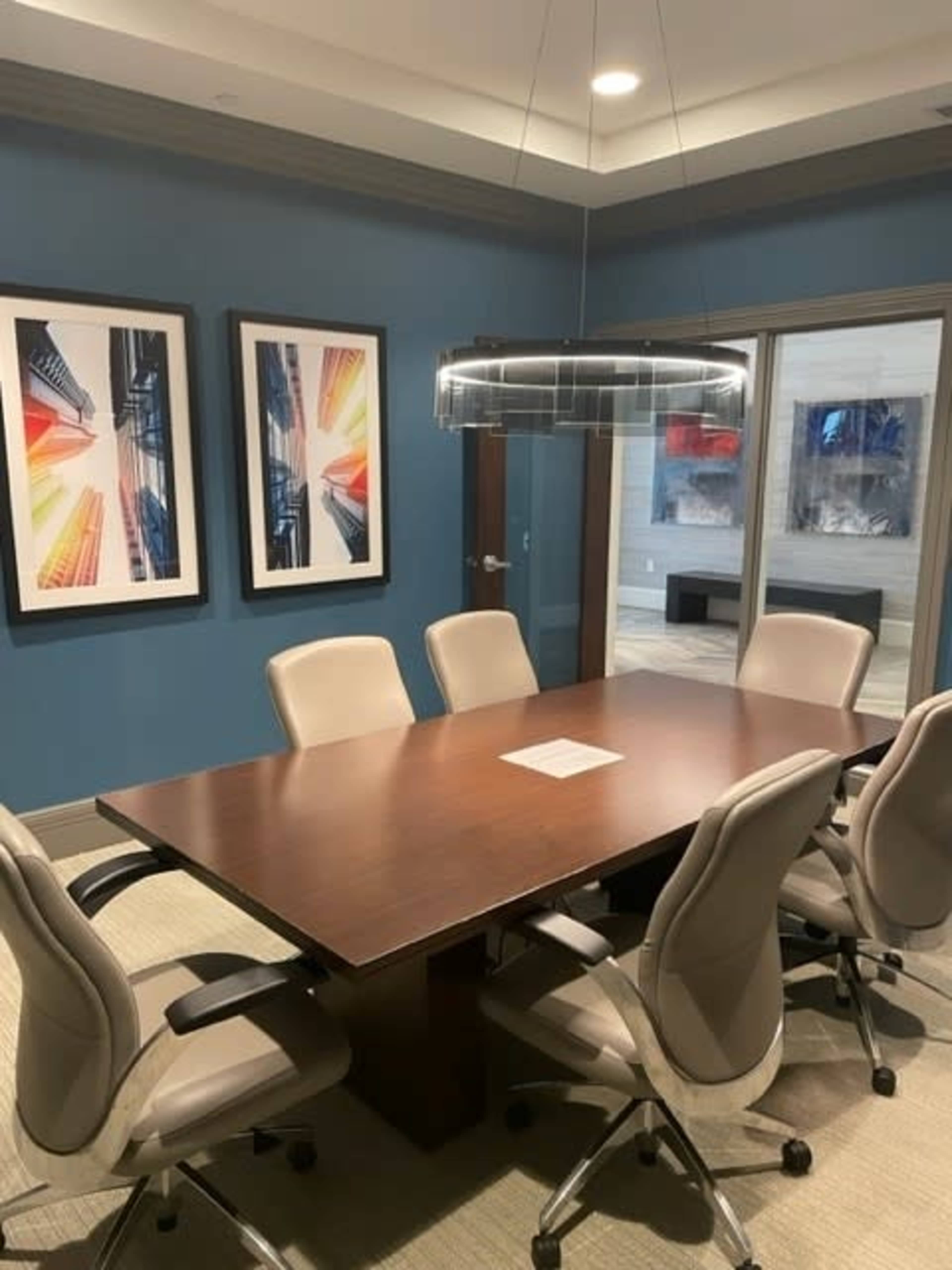 A modern conference room features a wooden table surrounded by ergonomic chairs and two large framed artworks on the walls.