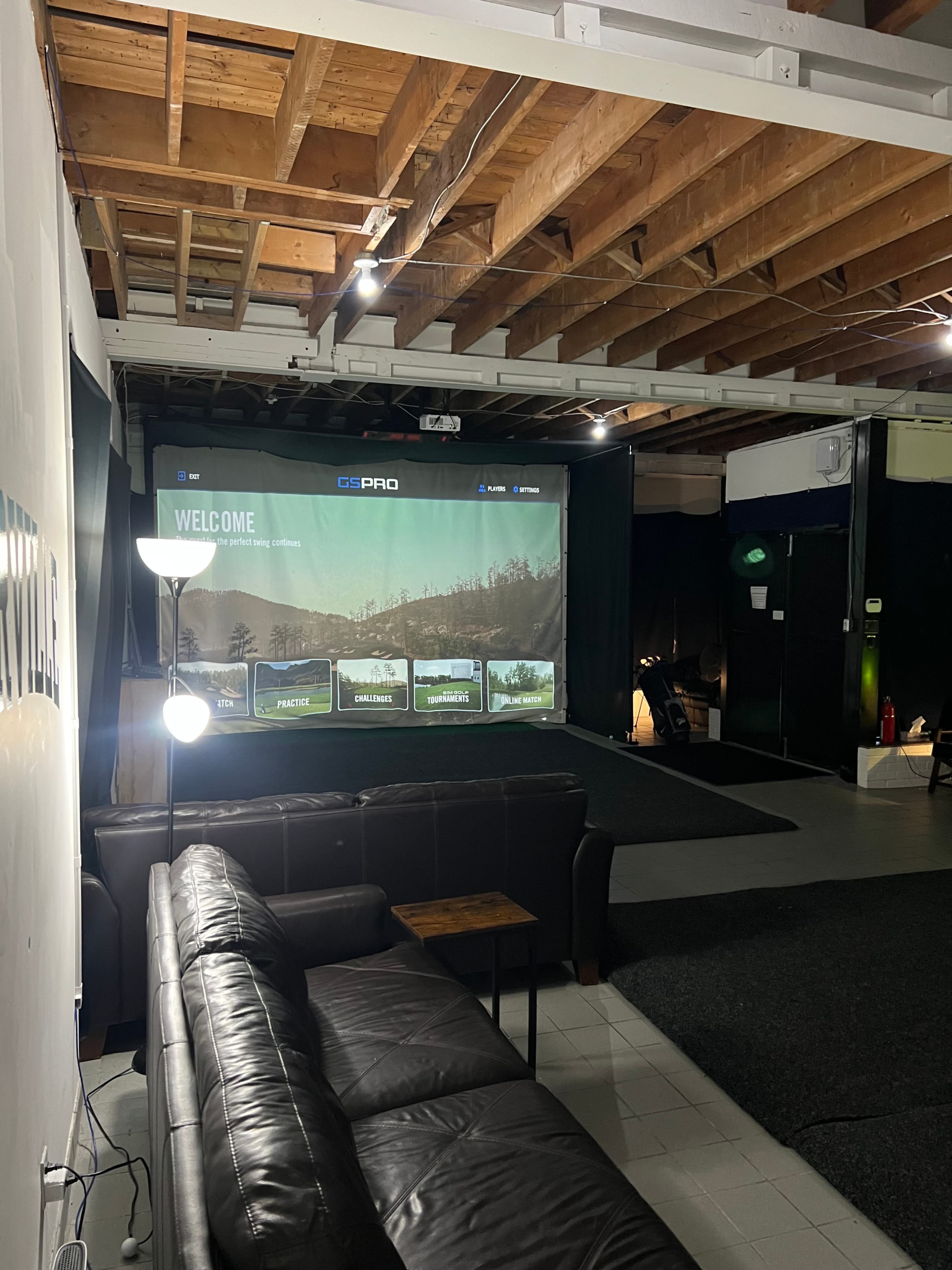 The image shows an interior space with a large screen displaying a welcome message, a dark couch, and a lamp in a partially illuminated room.