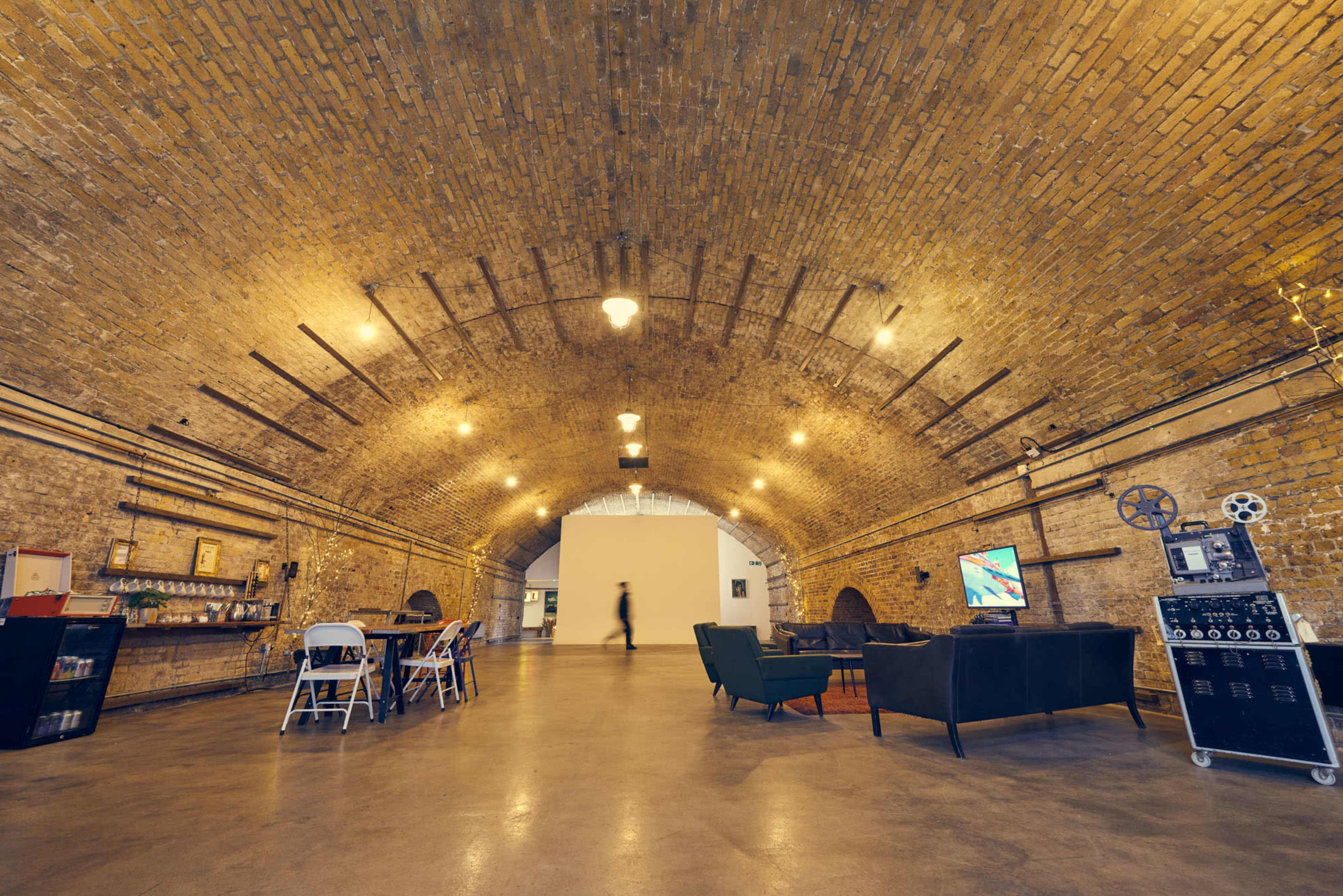 An arched brick interior featuring a seating area, a dining table, and a retro television setup against a backdrop of warm lighting.