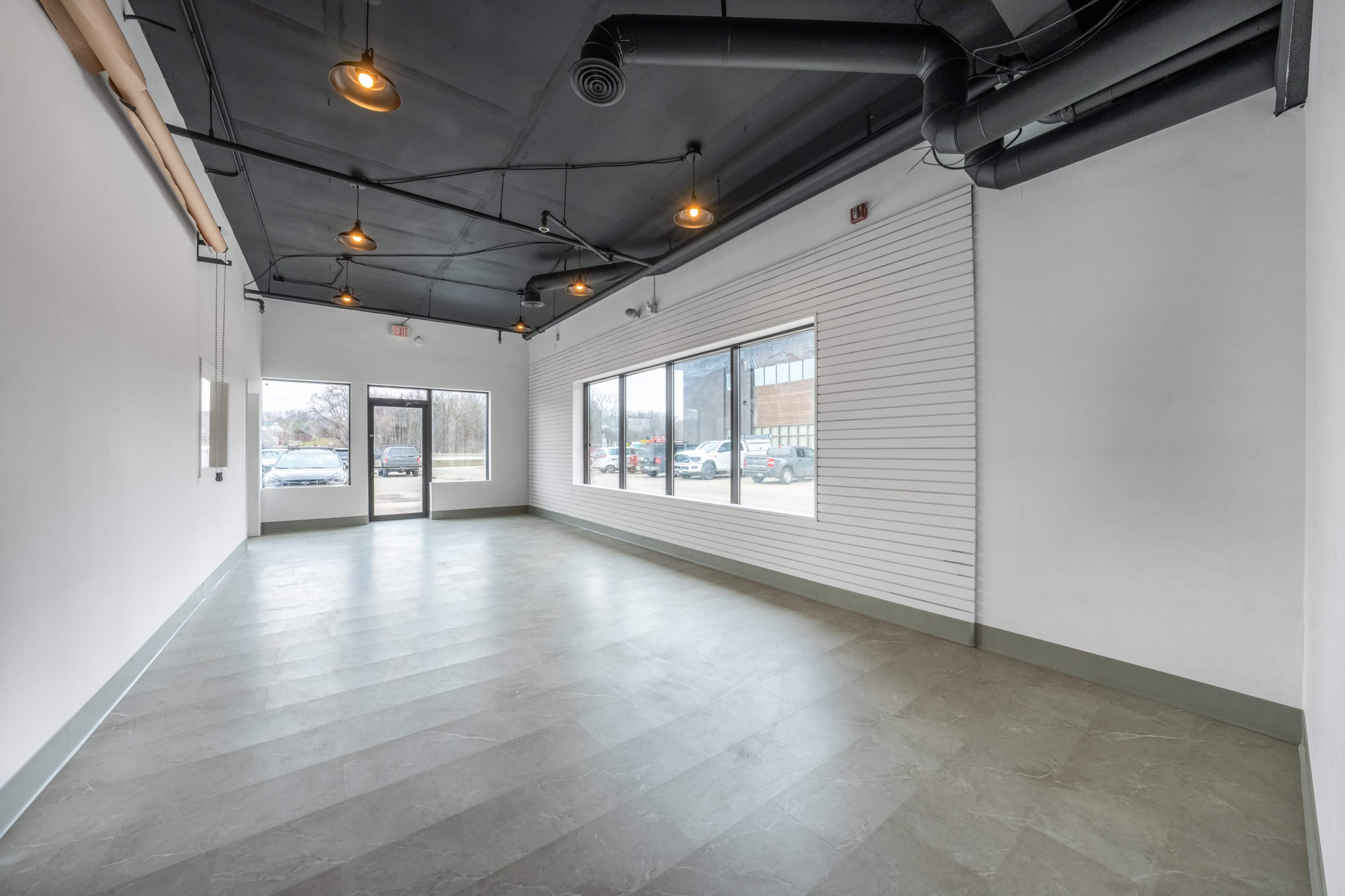 The image shows an empty retail space with large windows, concrete floors, and industrial-style lighting.