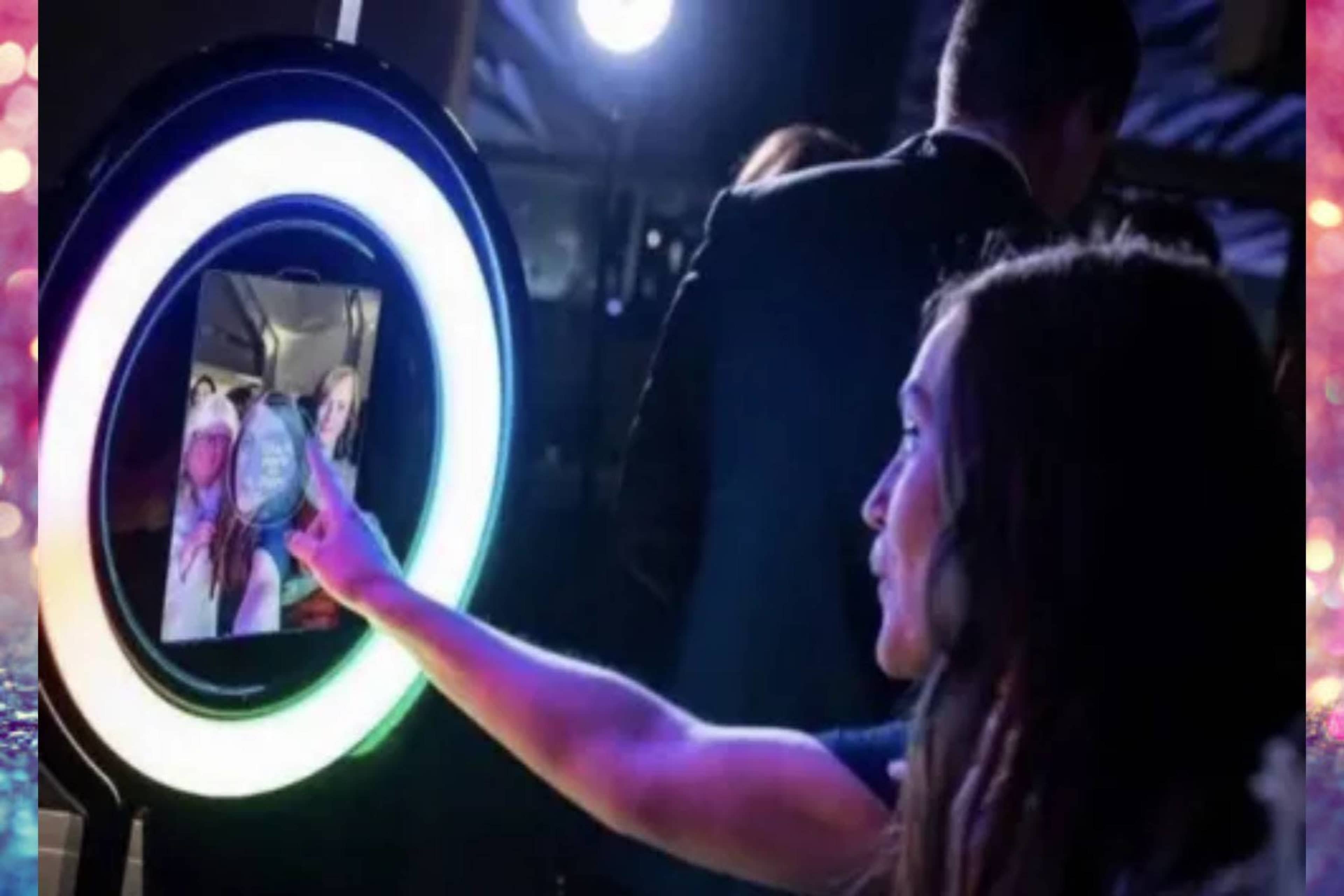 A woman interacts with a digital photo booth that features a circular illuminated frame.
