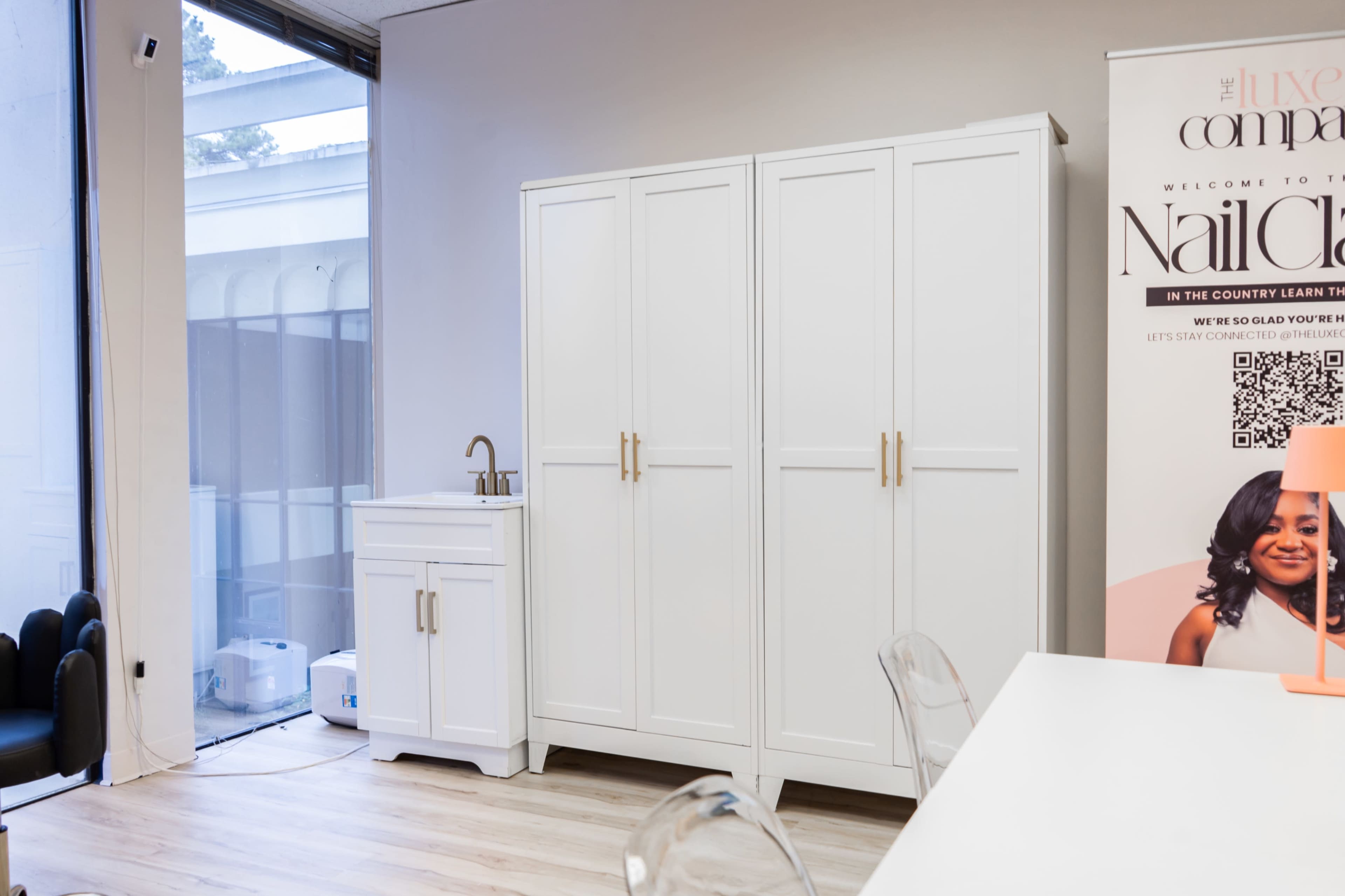 The image shows a bright room featuring a large white wardrobe and a smaller white sink cabinet next to a promotional banner for a nail salon.