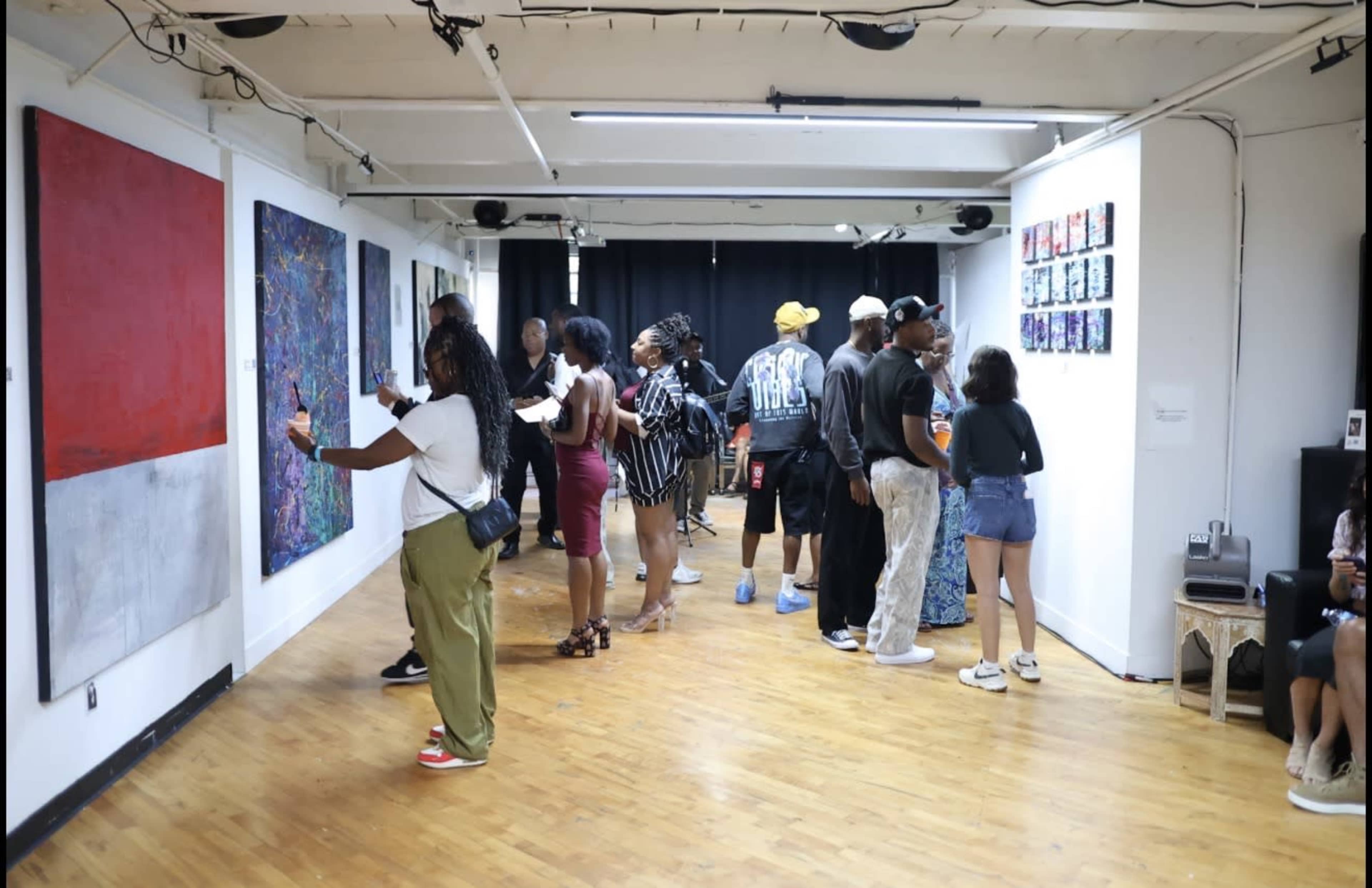 People are interacting and admiring artwork in a gallery space with a wooden floor and white walls.