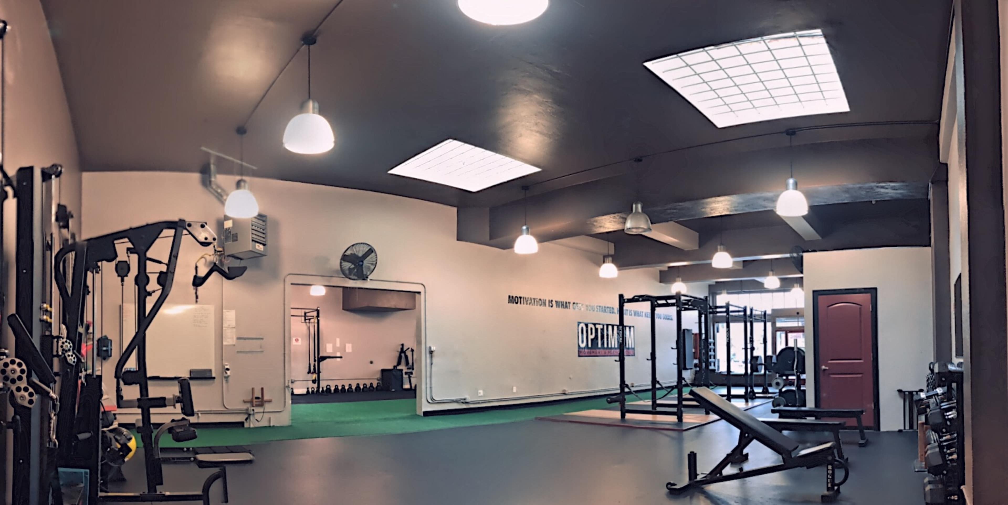 A spacious gym interior with workout equipment, bright overhead lighting, and a green turf area.