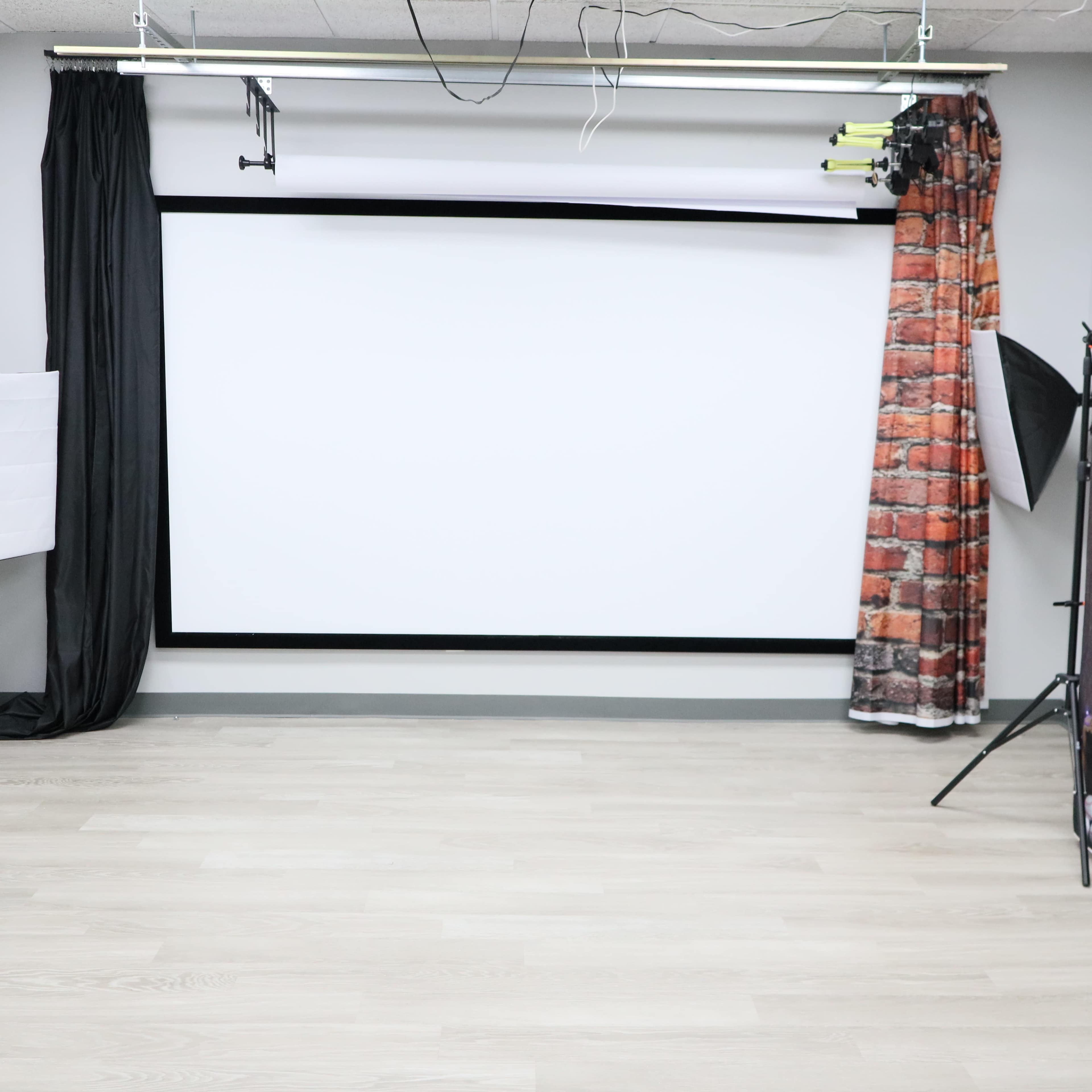 The image shows a large blank white projection screen set up in a room with light wood flooring and minimal decorations.
