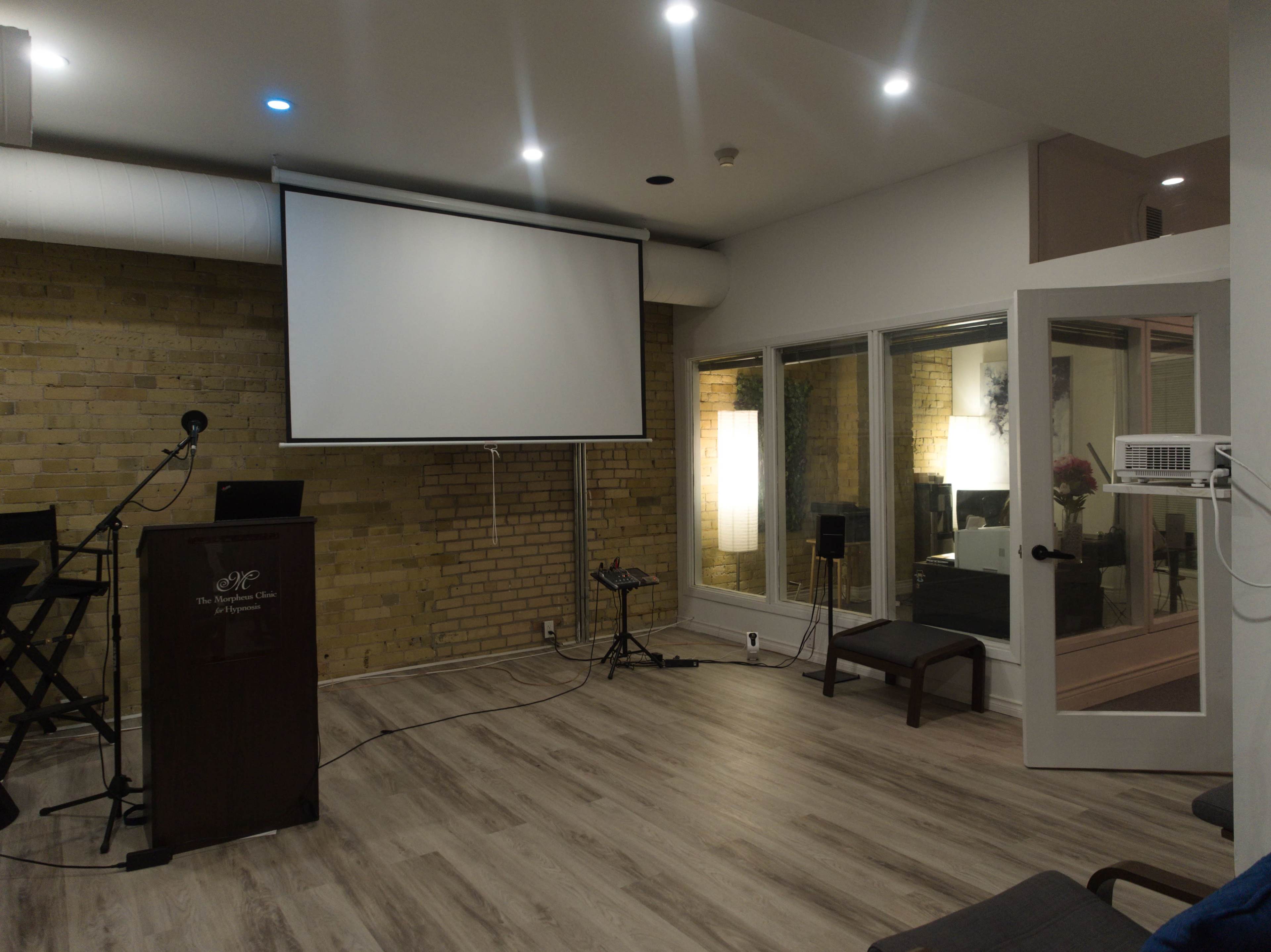 A modern conference room with a projector screen, a podium, and large windows providing natural light.