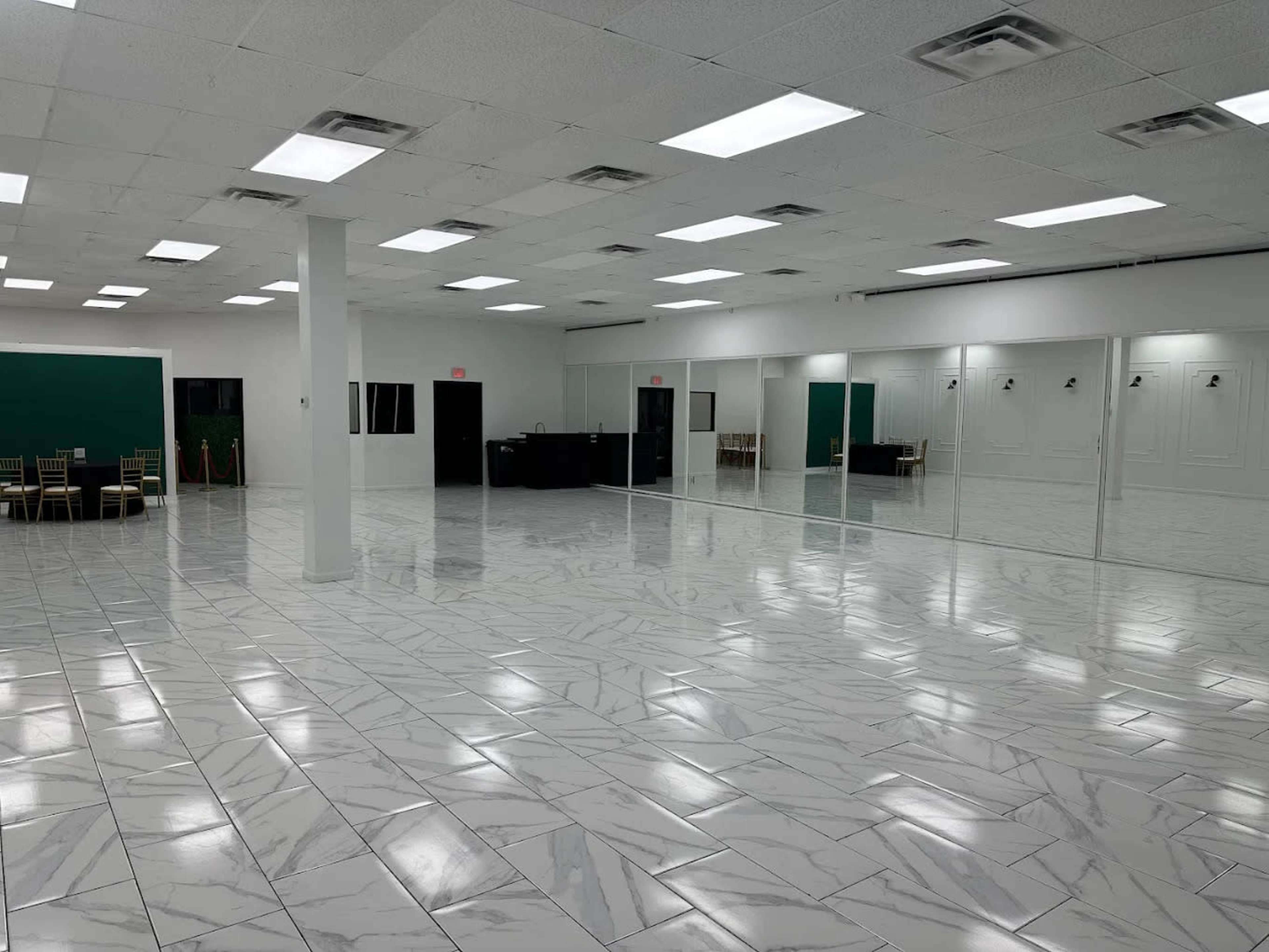 The image shows a spacious, empty room with glossy white marble flooring, bright overhead lights, and large mirrors lining one wall.