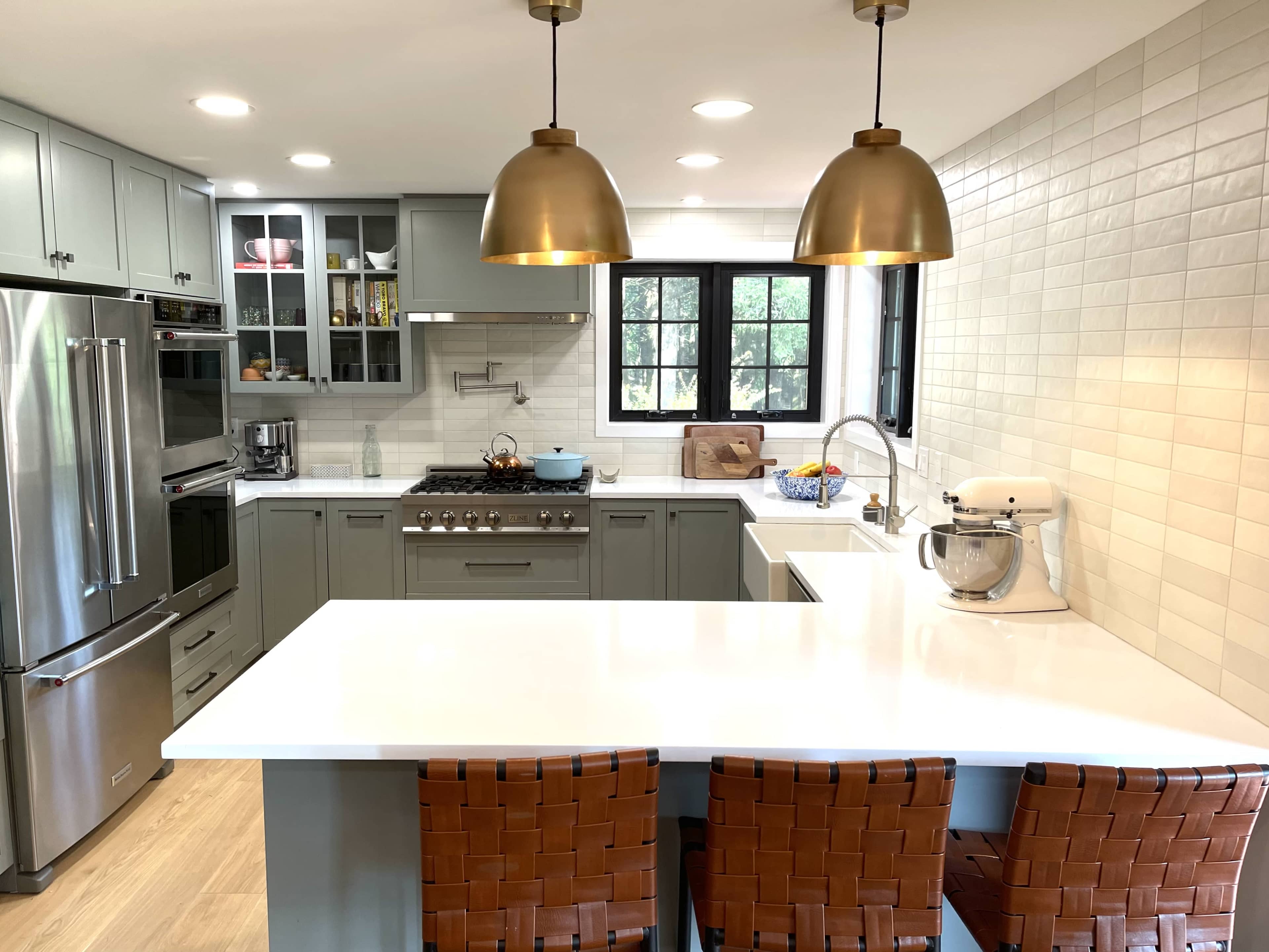 A modern kitchen features gray cabinetry, a large island with three woven bar stools, and stainless steel appliances, including a gas stove and a stand mixer.