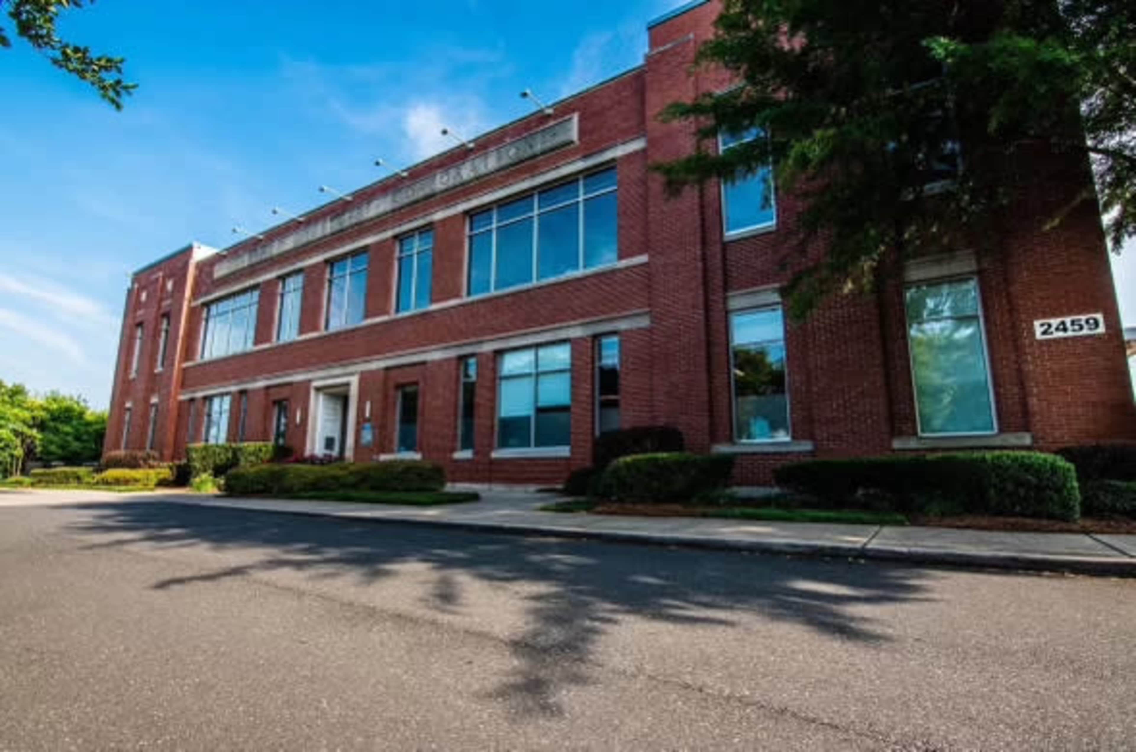 The image shows a brick building with large windows and a parking area in front, labeled "2459."