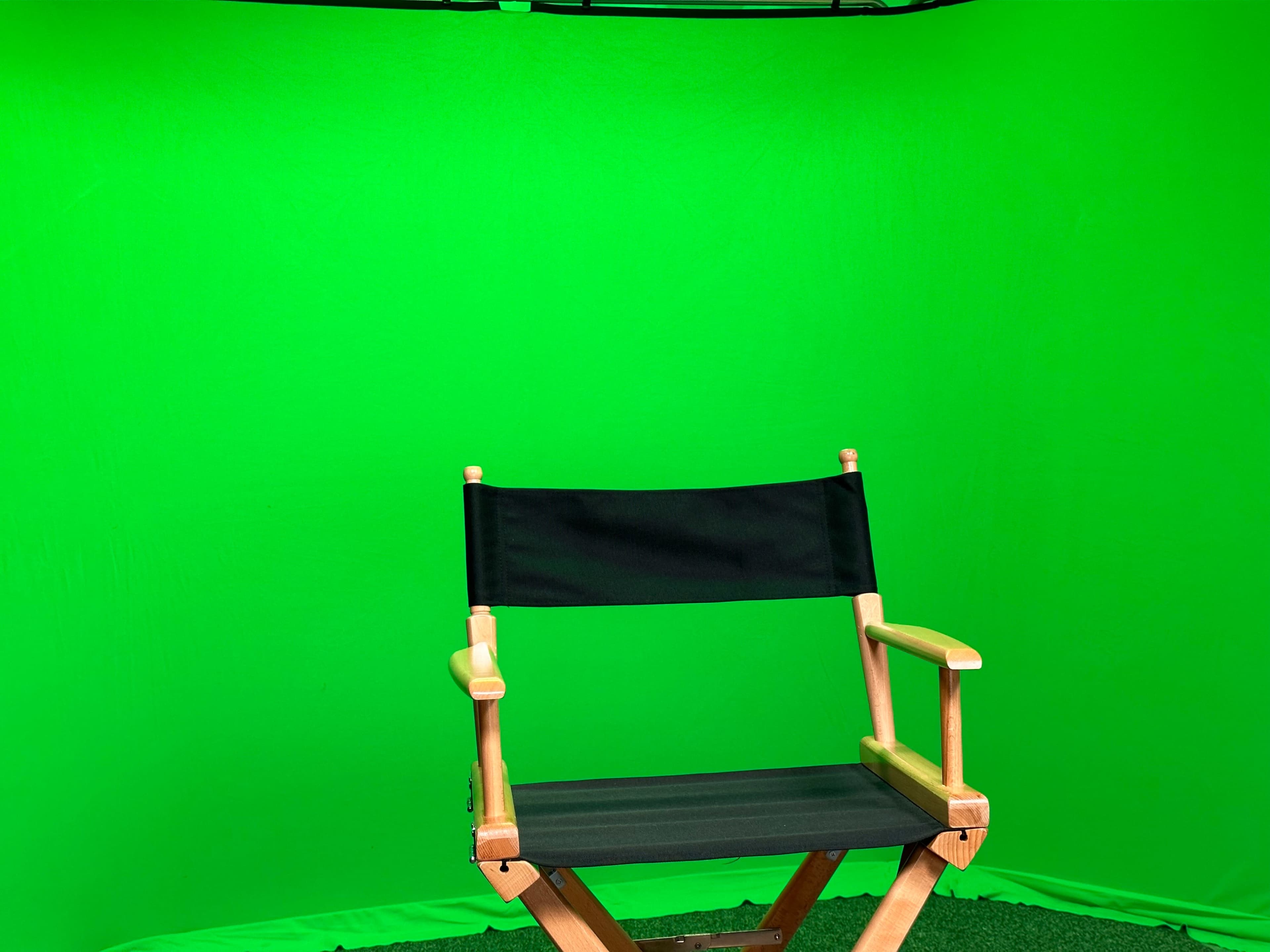 A black director's chair is positioned in front of a green backdrop.