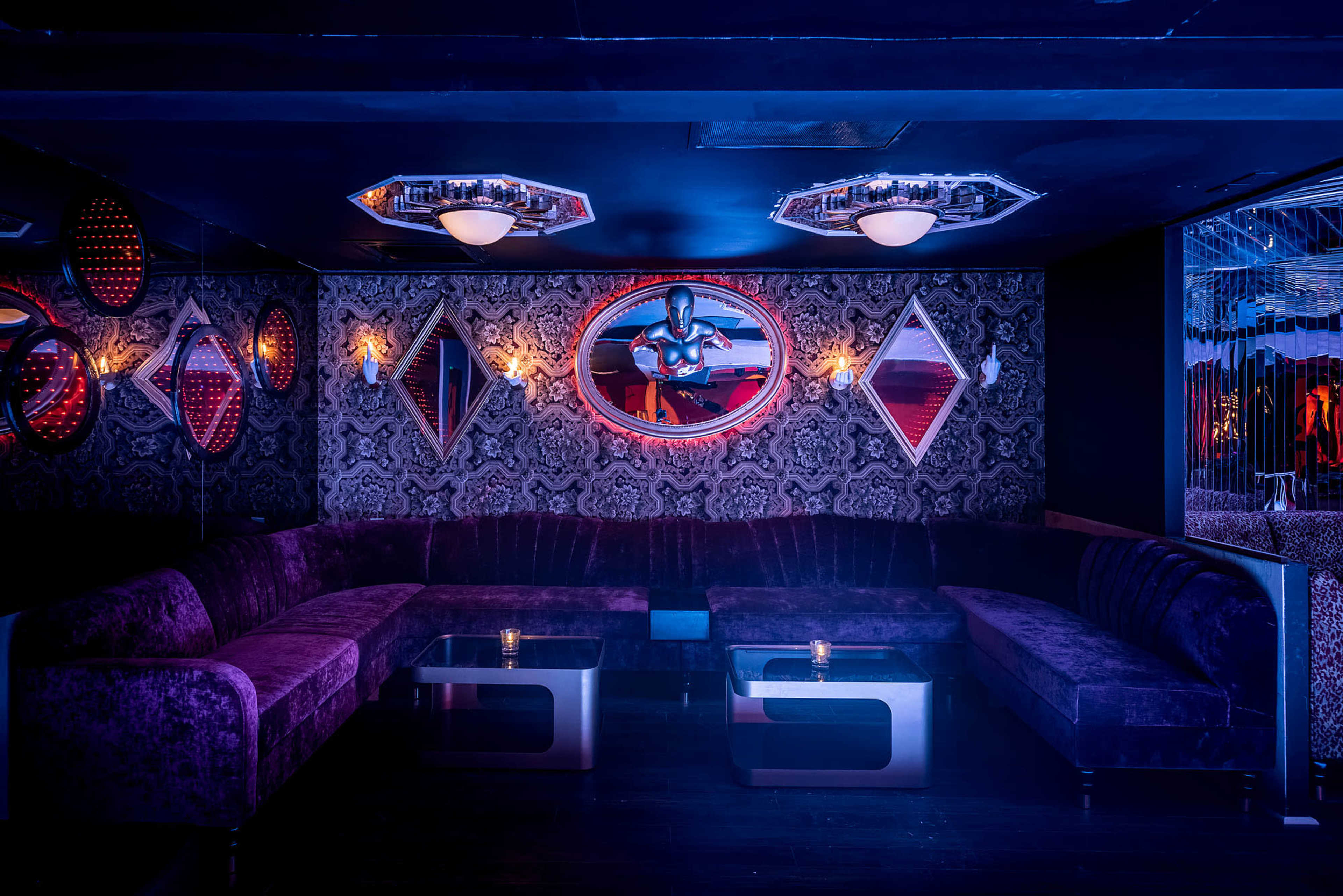 A plush, dimly-lit lounge area features a velvet seating arrangement and decorative mirrors on the walls.