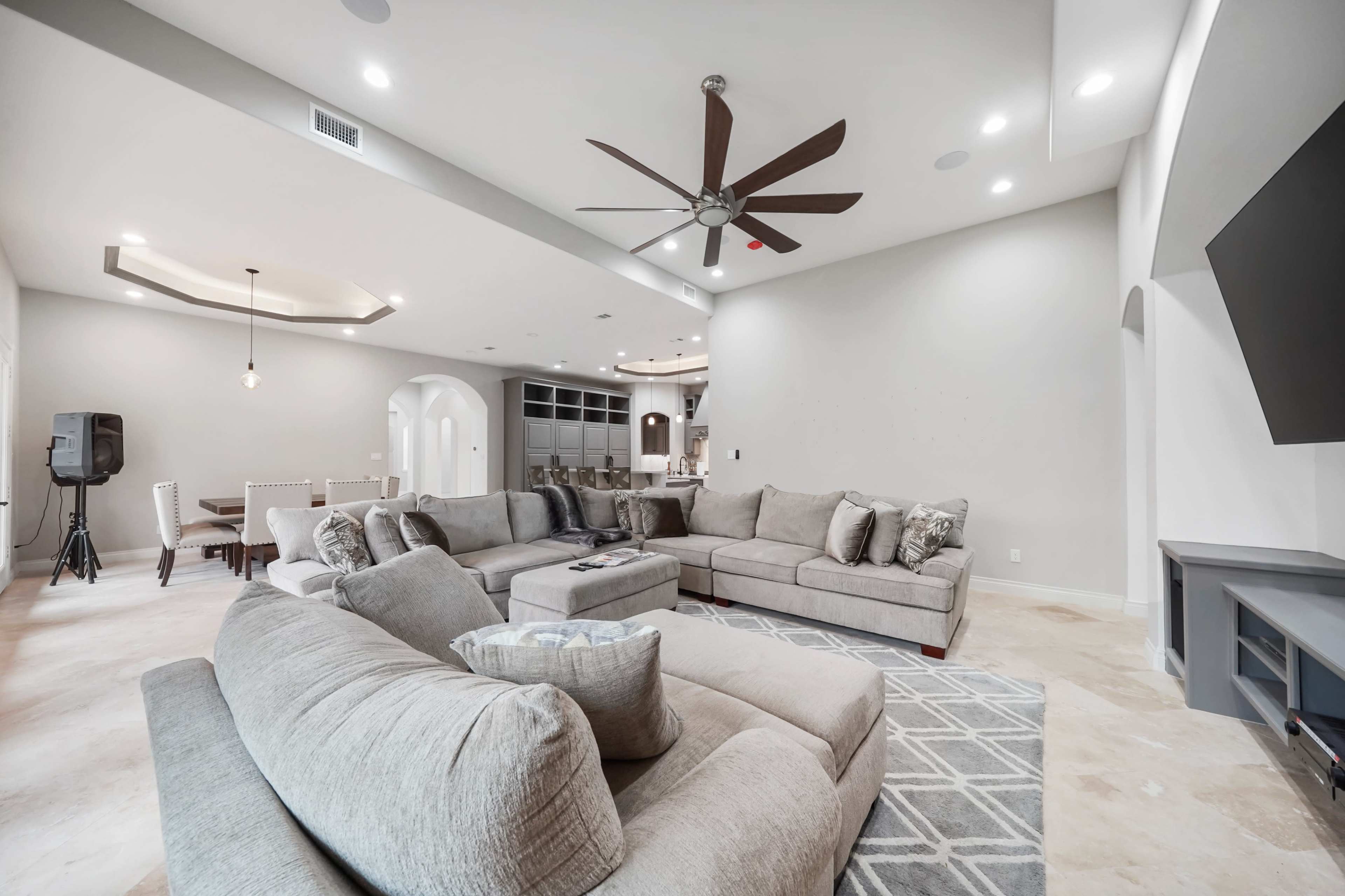 A spacious living room with a gray sectional sofa, a ceiling fan, and a view of a dining area in the background.