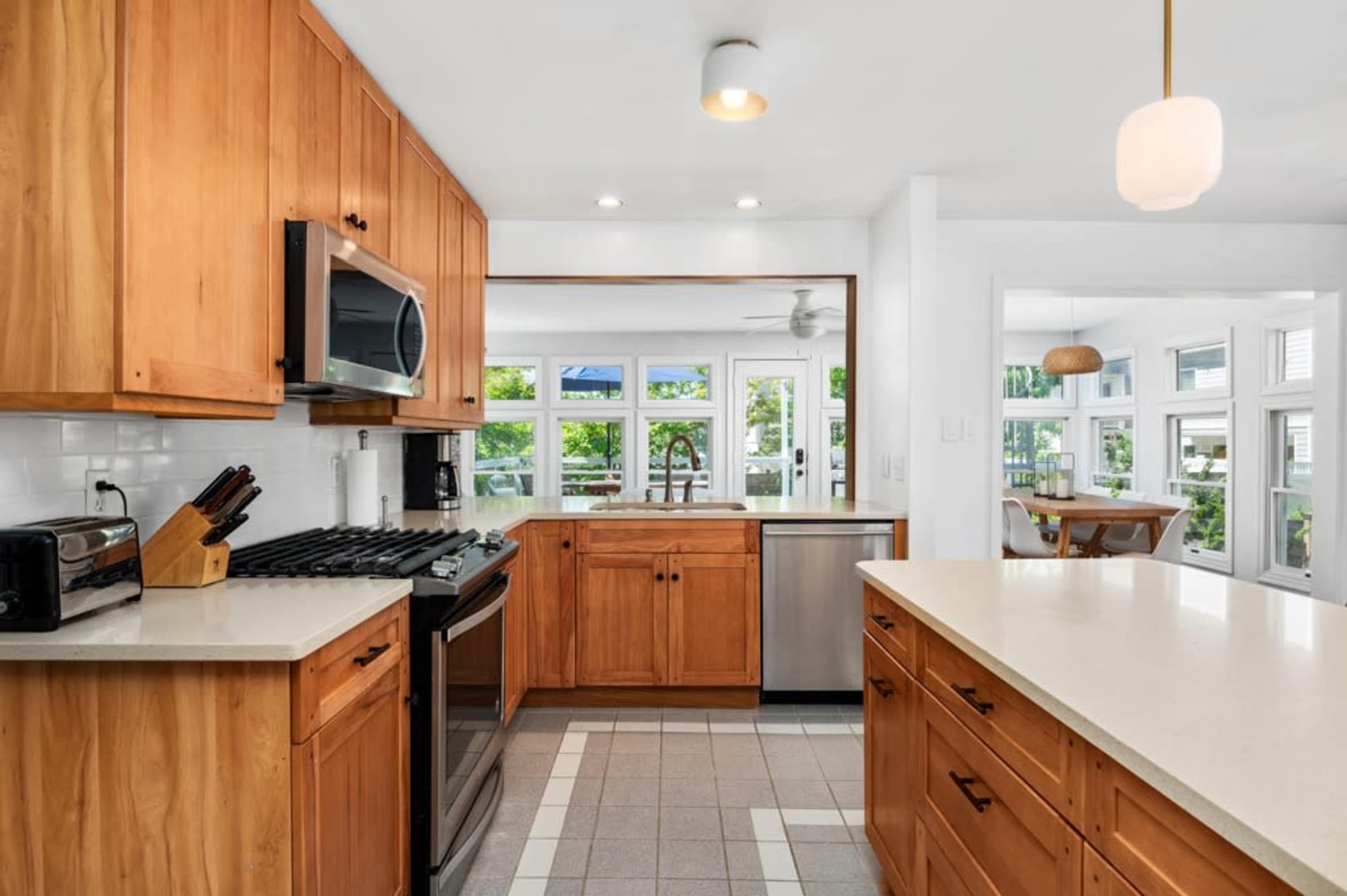 The kitchen features wooden cabinetry, stainless steel appliances, and a spacious layout with a view into a bright dining area.