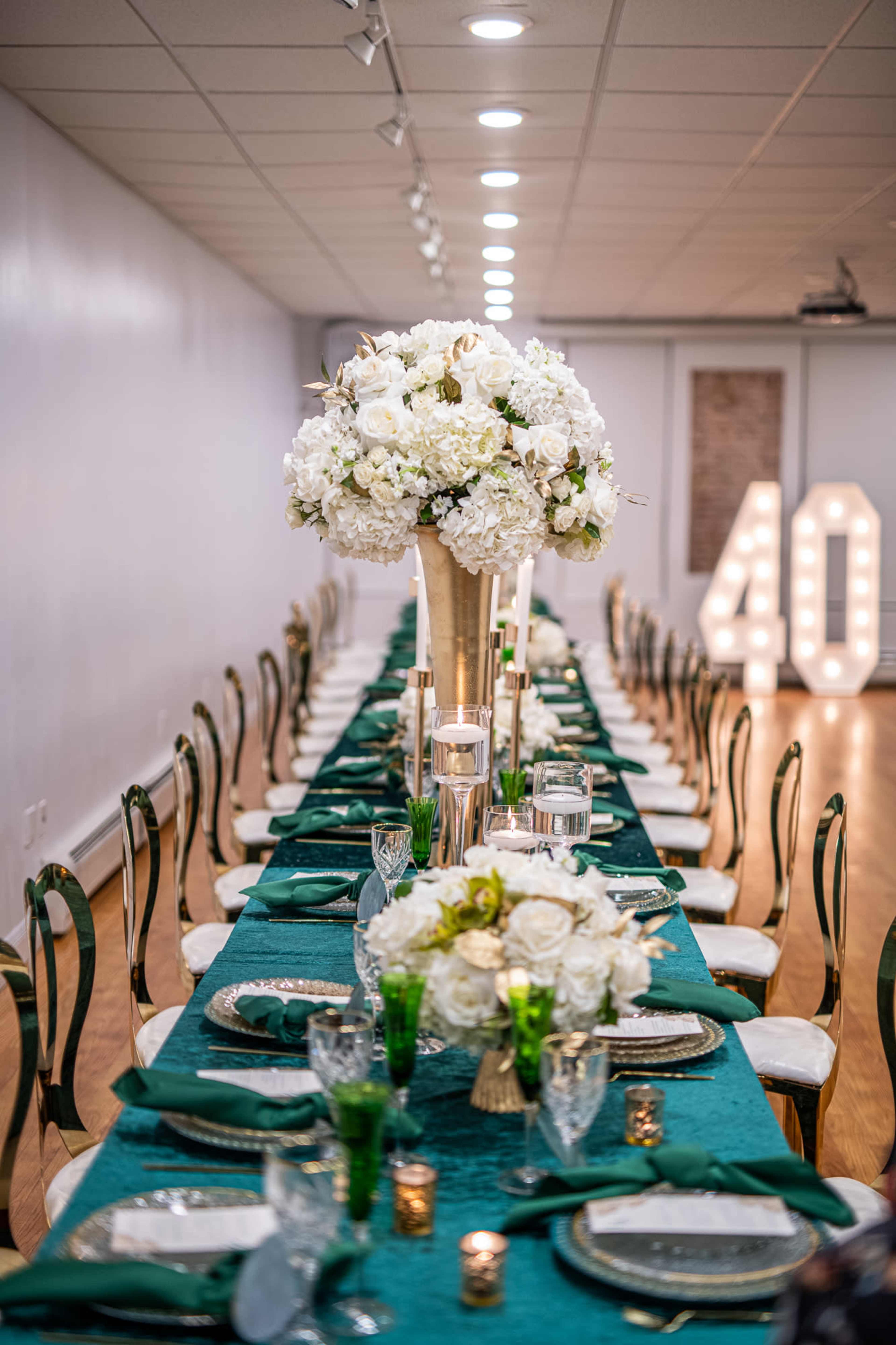 A long banquet table is set with green tablecloths, white floral centerpieces, and decorative candles, with large illuminated numbers "40" in the background.