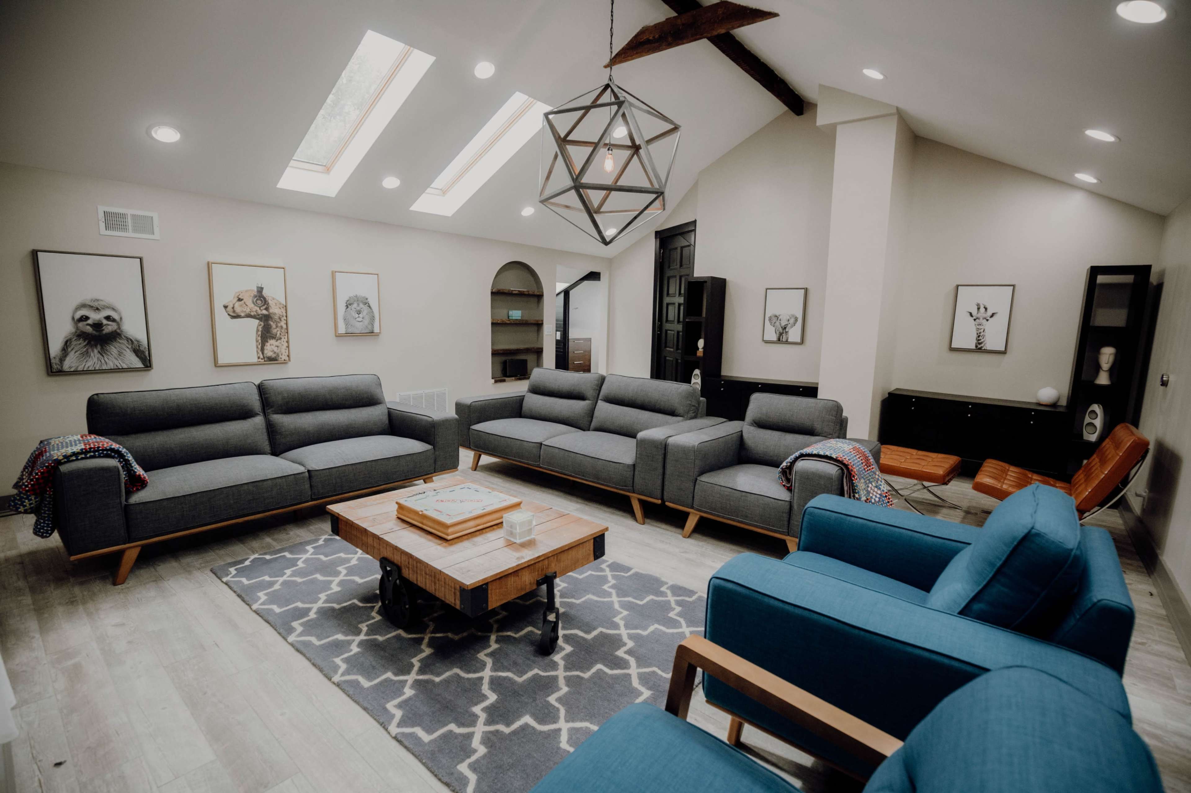 The room features a modern living area with gray sofas, blue armchairs, a wooden coffee table, and framed animal artwork on the walls.