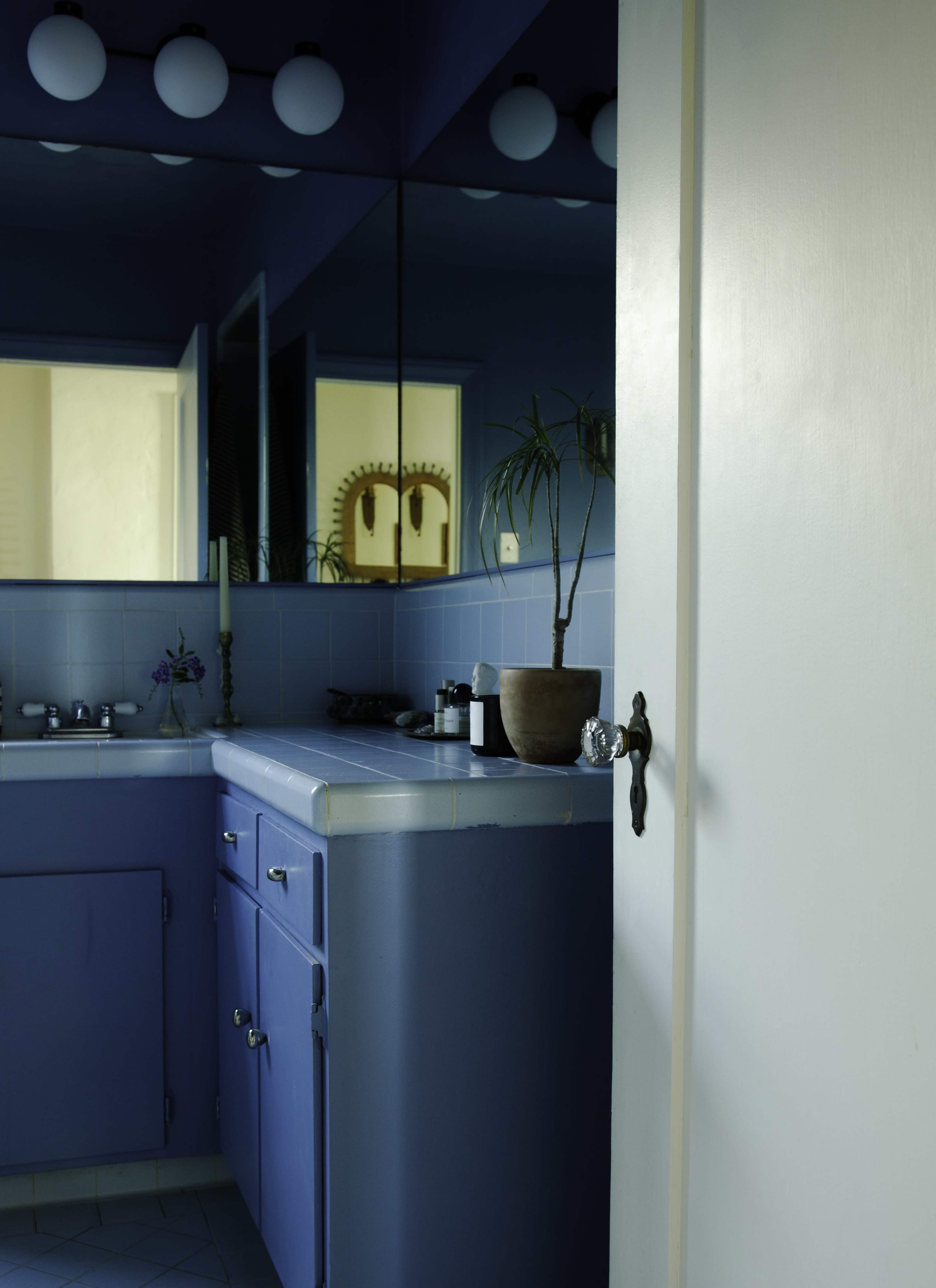 The image shows a bathroom with blue walls, a blue countertop, and a mirror reflecting a plant and decor.