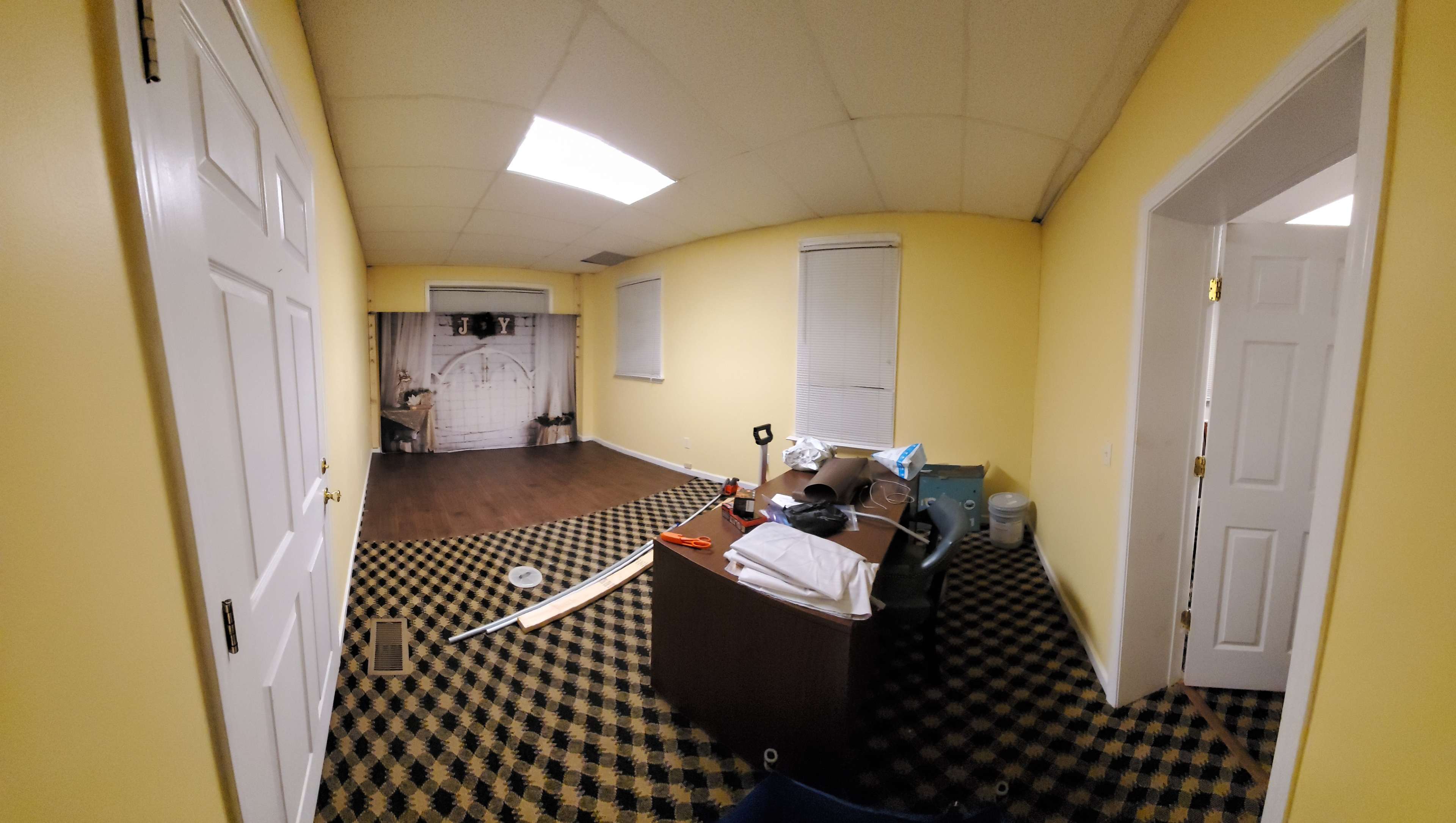 An empty room with yellow walls, a black and yellow checkered floor, a large desk, and a backdrop featuring a grid pattern.